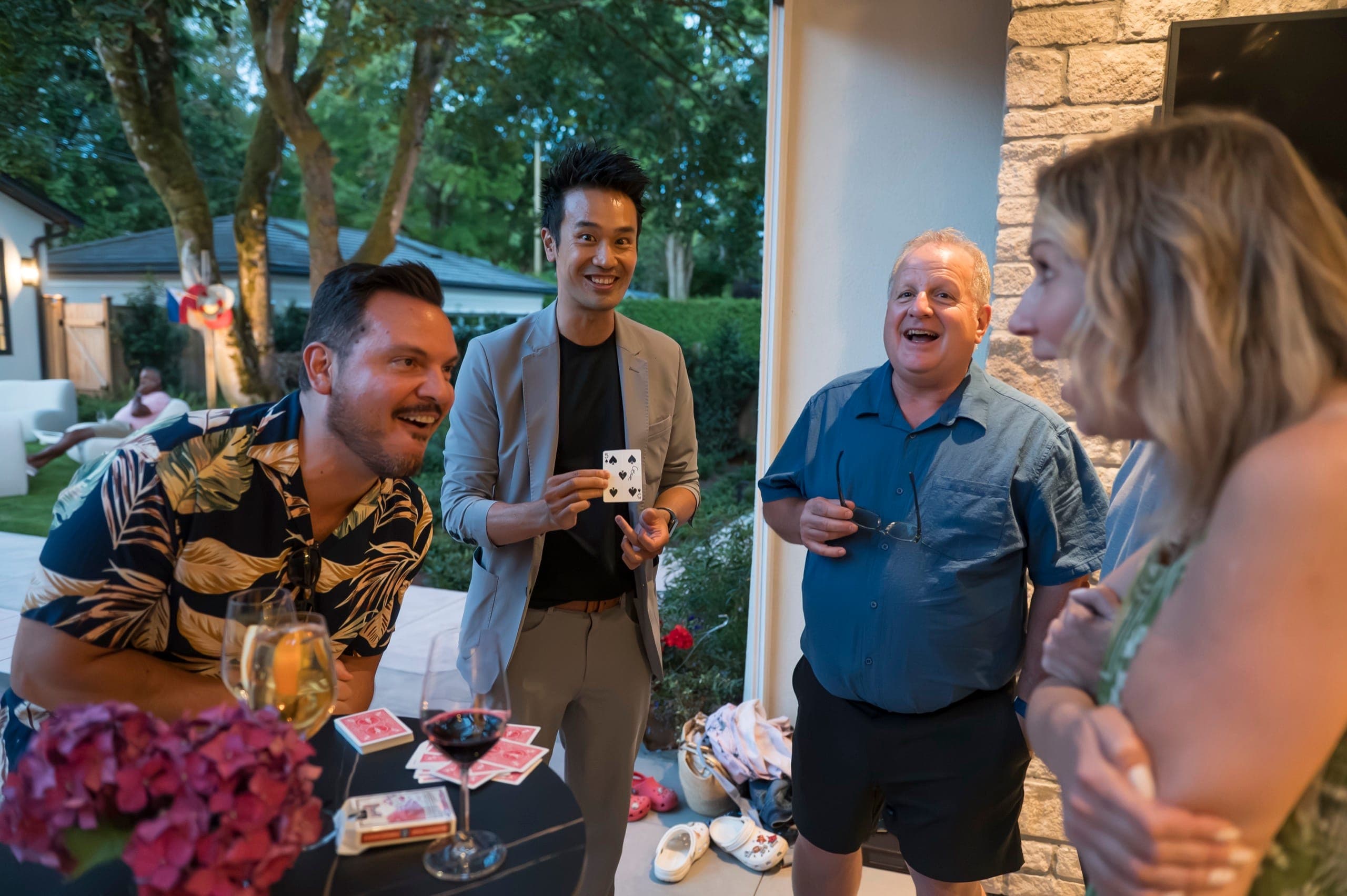 A group gathered around a cocktail table laughing together during close-up magic at a private Vancouver party