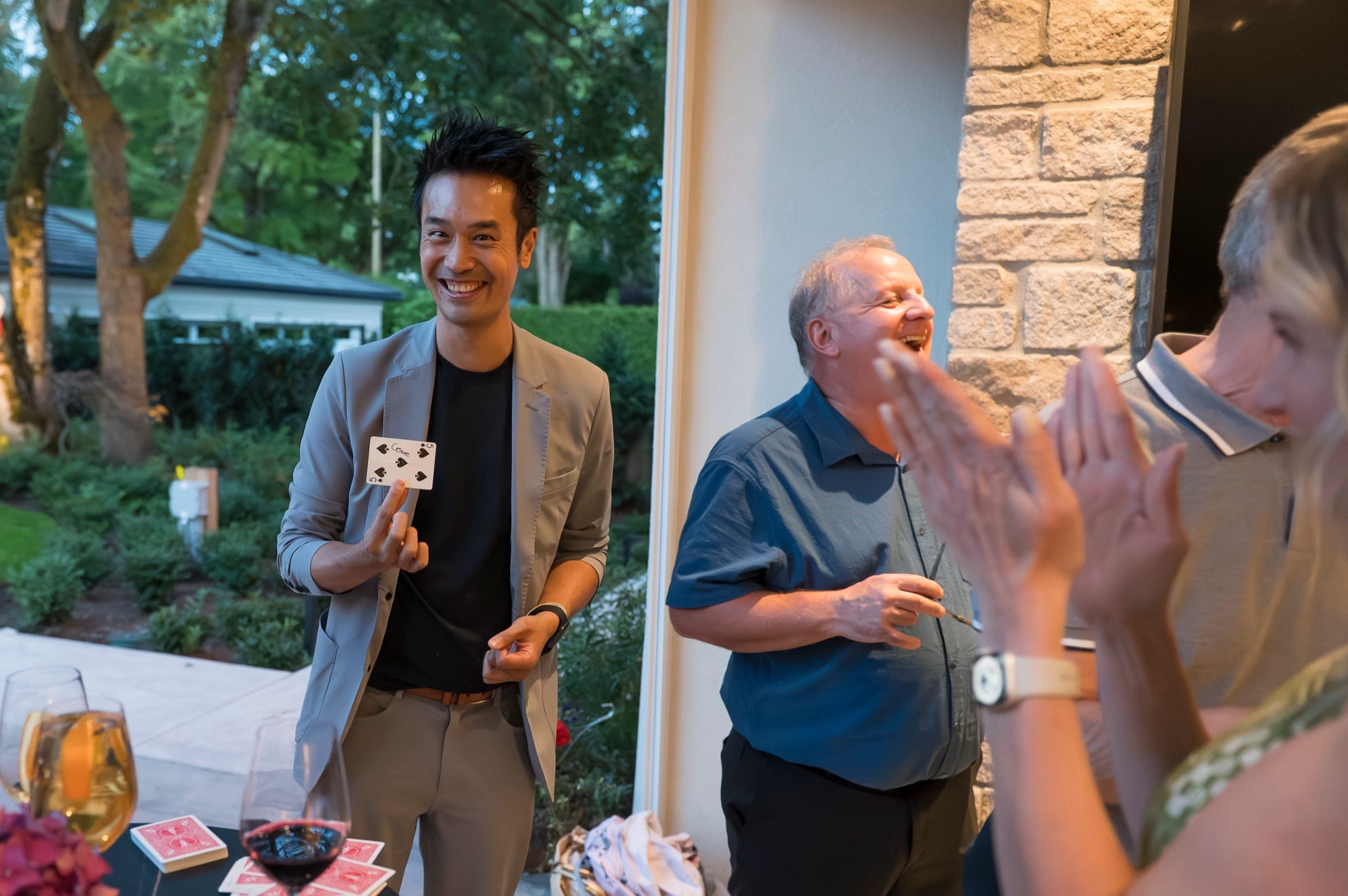 Kel holding up a chosen card while guests around the table laugh and applaud at a private Vancouver party