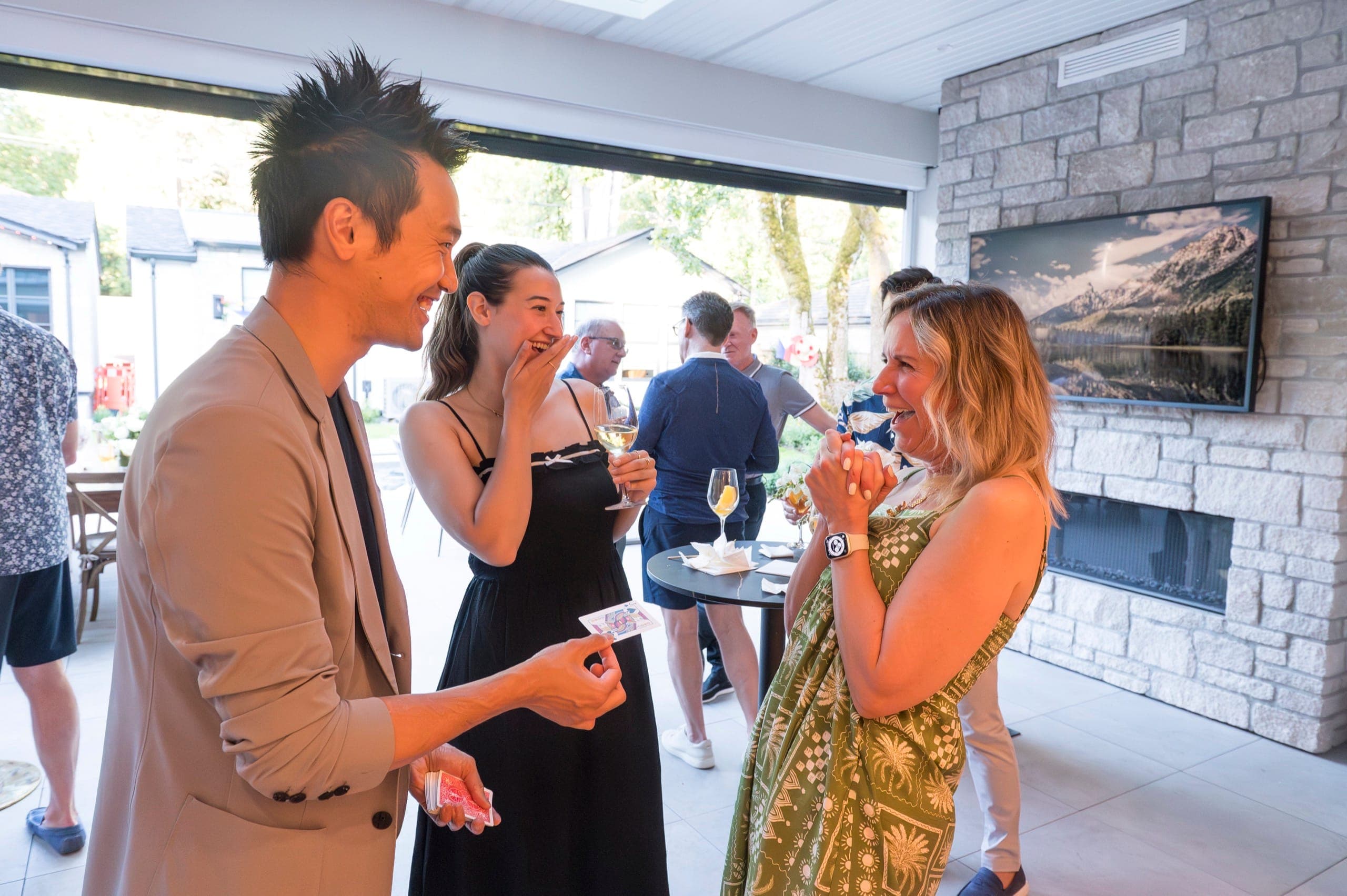 Two women reacting at once during close-up magic at a private Vancouver party, one with her hand over her mouth