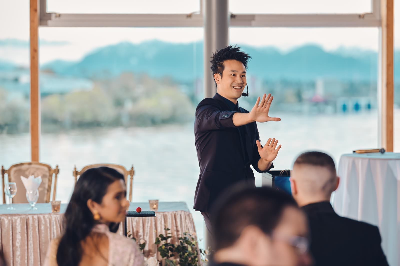 Kel performing in front of the windows at the UBC Boathouse, with the river and mountains behind him