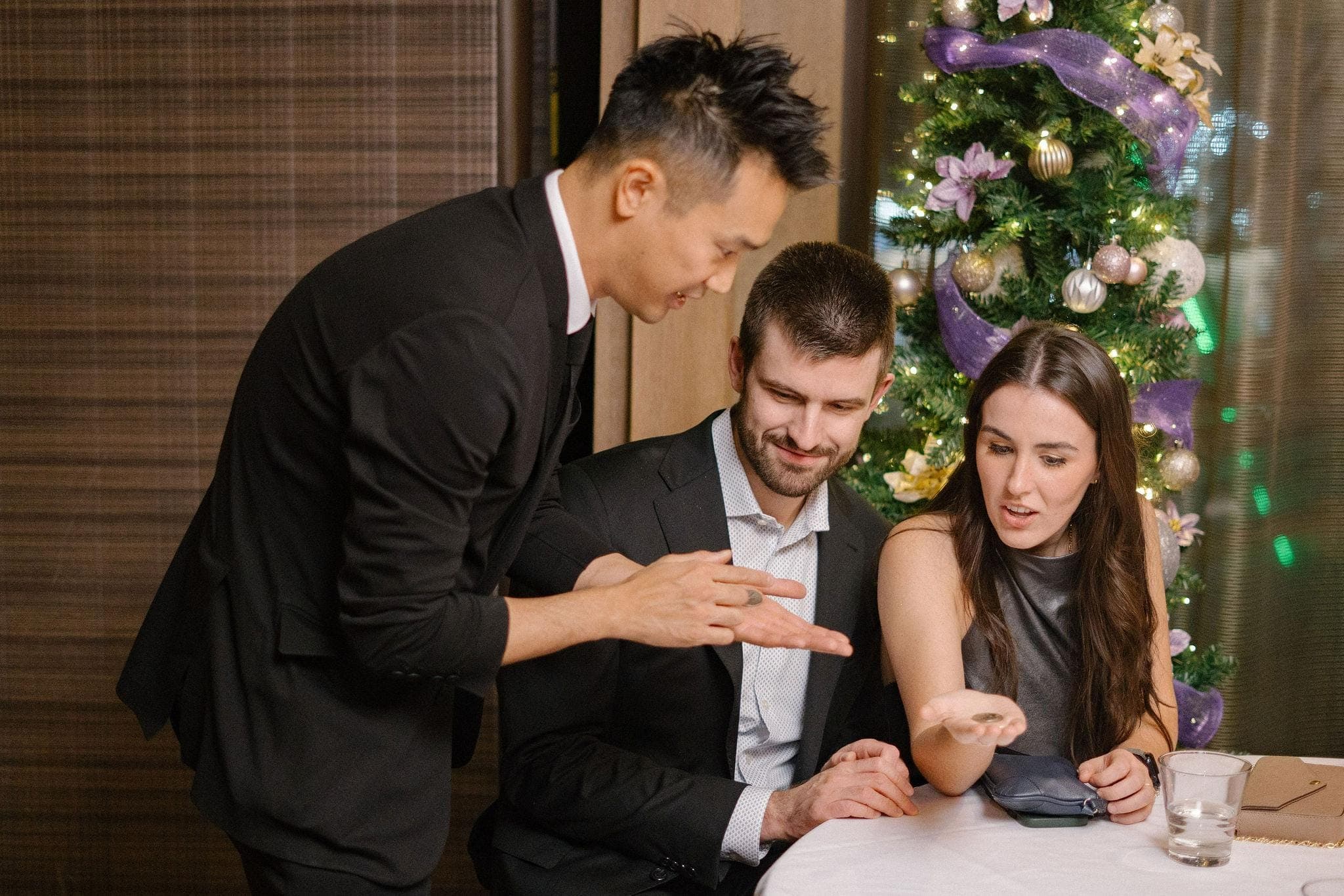 Kel performing a coin routine for two guests beside the Christmas tree at a Vancouver law firm holiday party