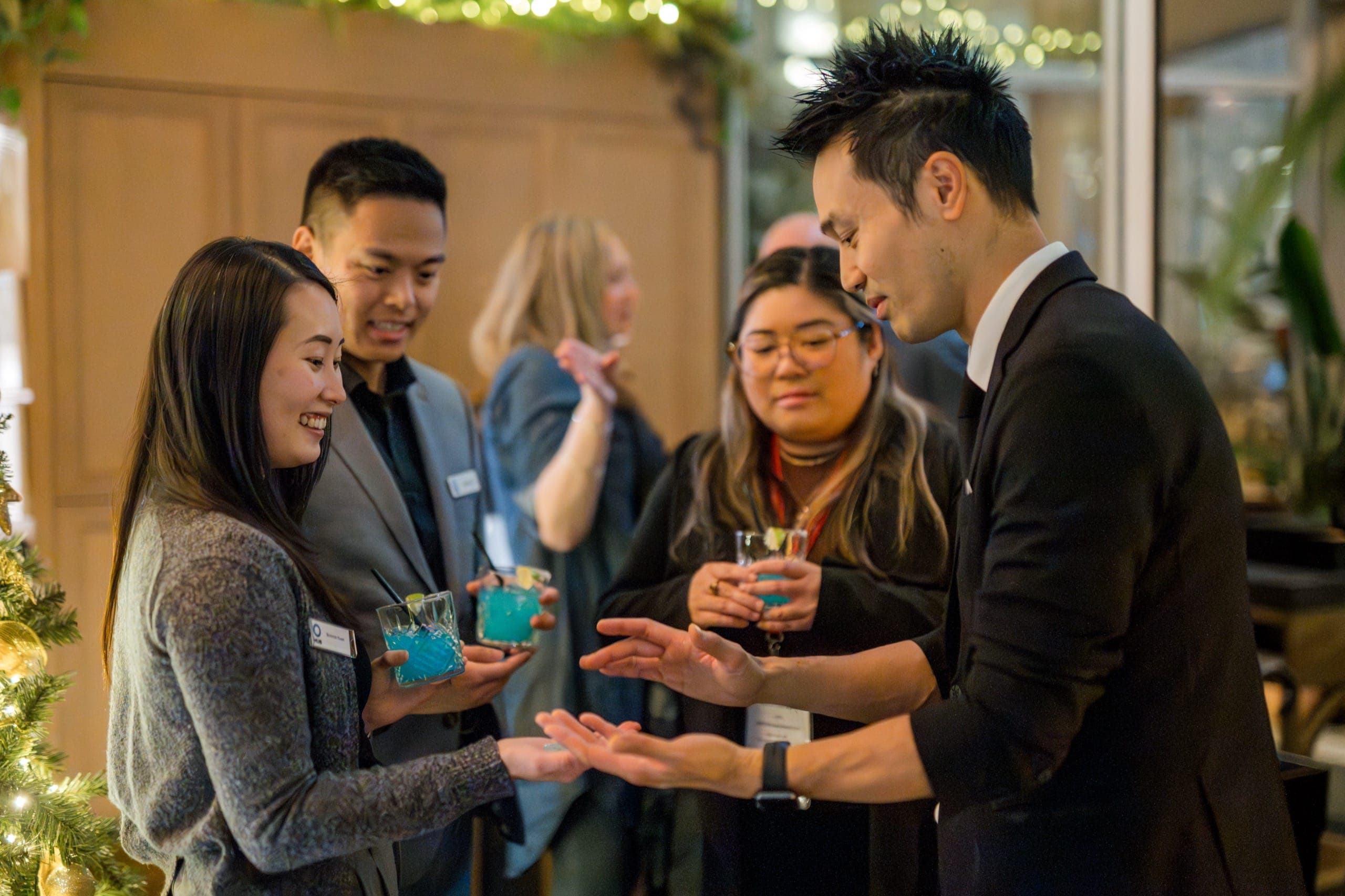 Kel resting a coin on a guest's open palm while three guests watch during a formal reception