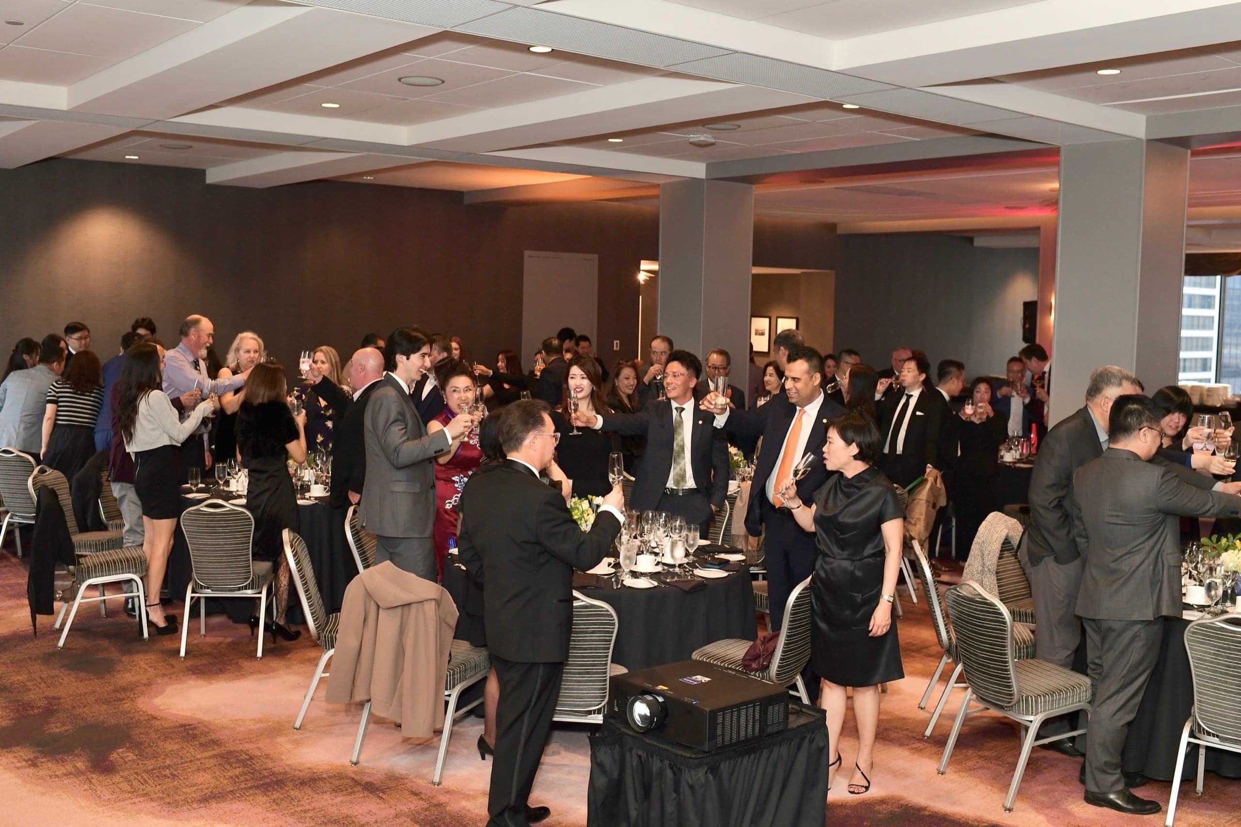 A full ballroom of guests standing with glasses raised for a toast at a Vancouver fundraiser evening