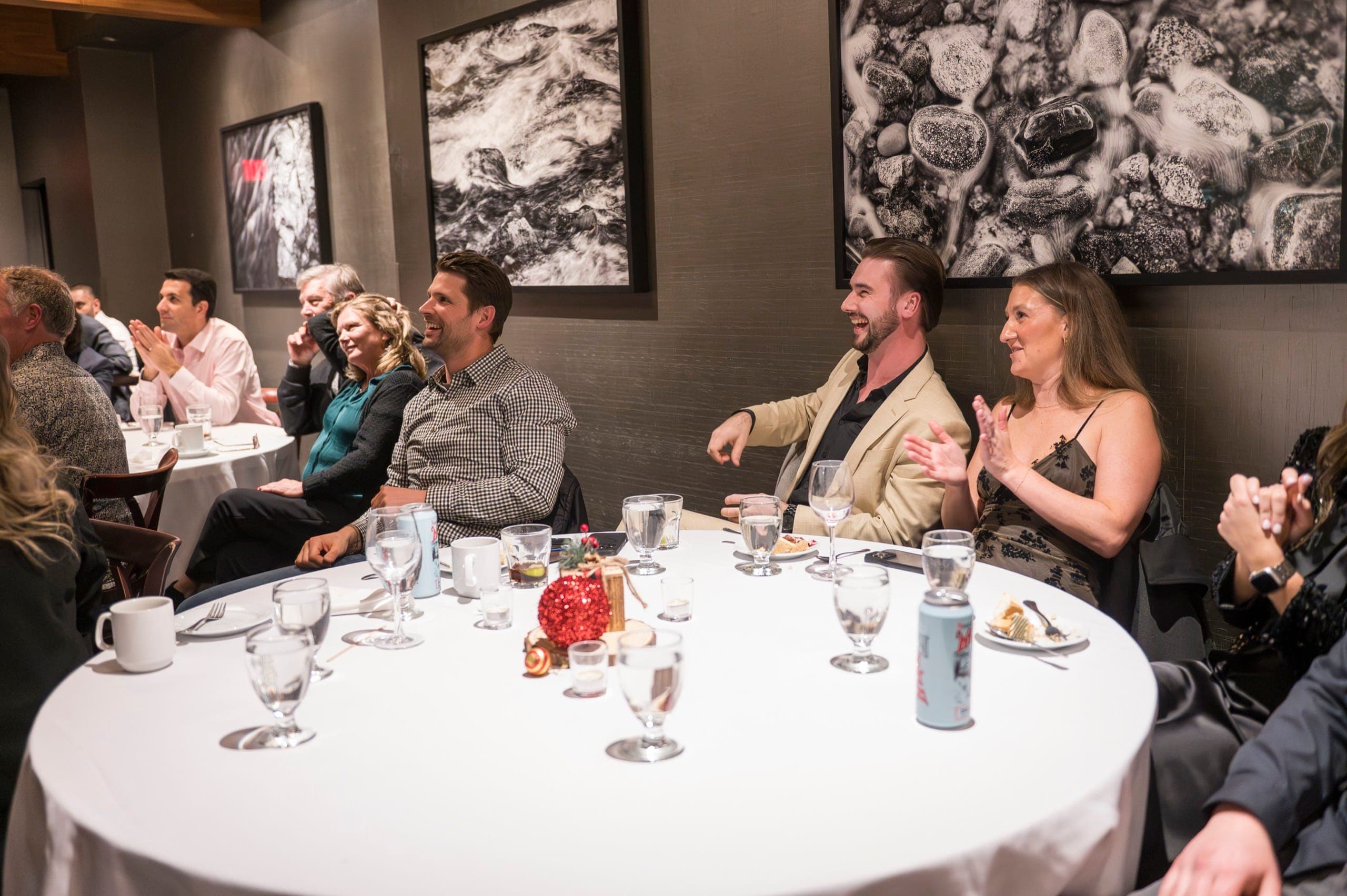A full room of corporate guests laughing and applauding at their tables during a Vancouver event