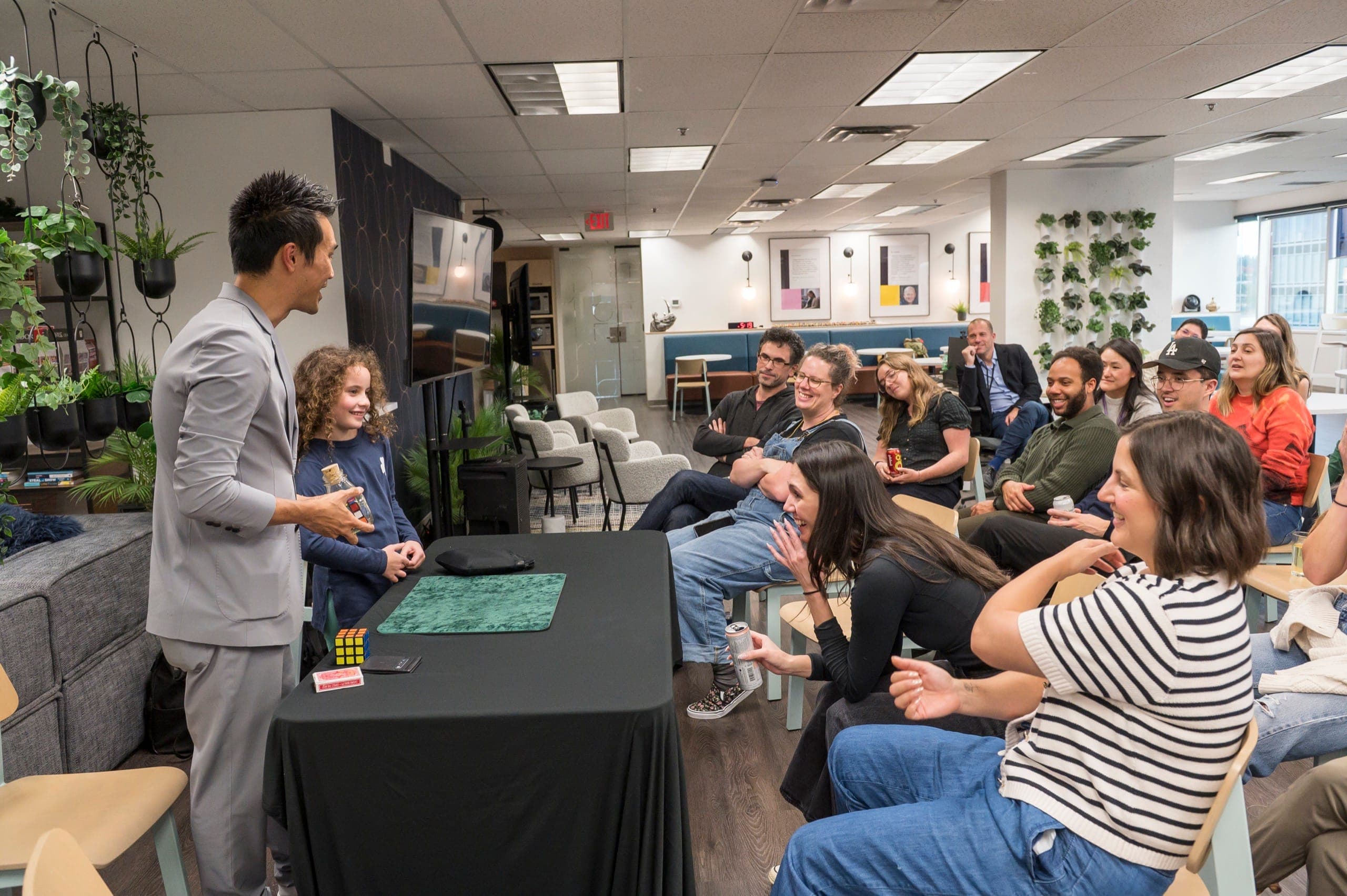 A seated audience laughing hard while Kel works with a volunteer at a corporate event