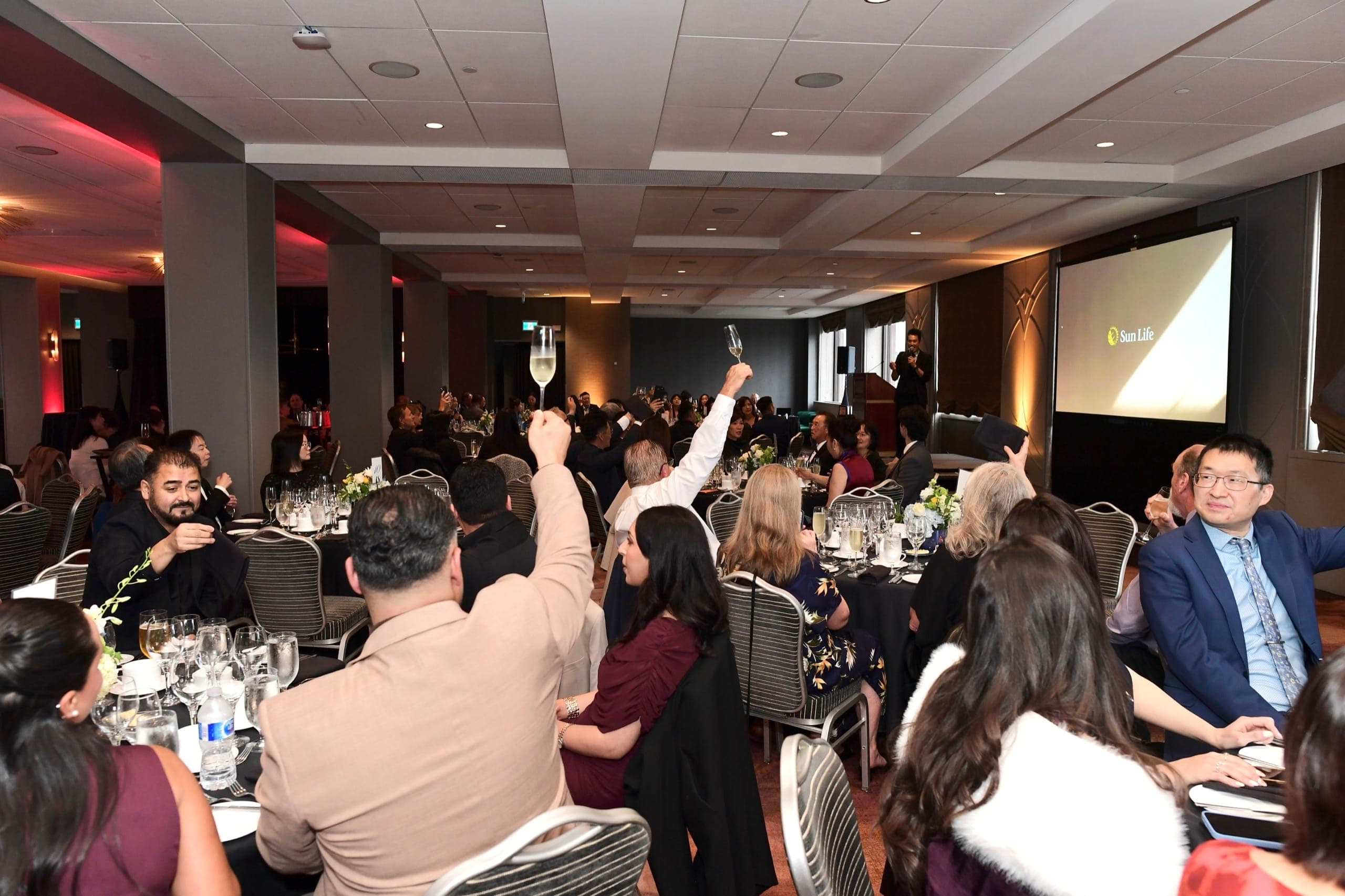 A room of guests raising glasses for a toast during a corporate evening event