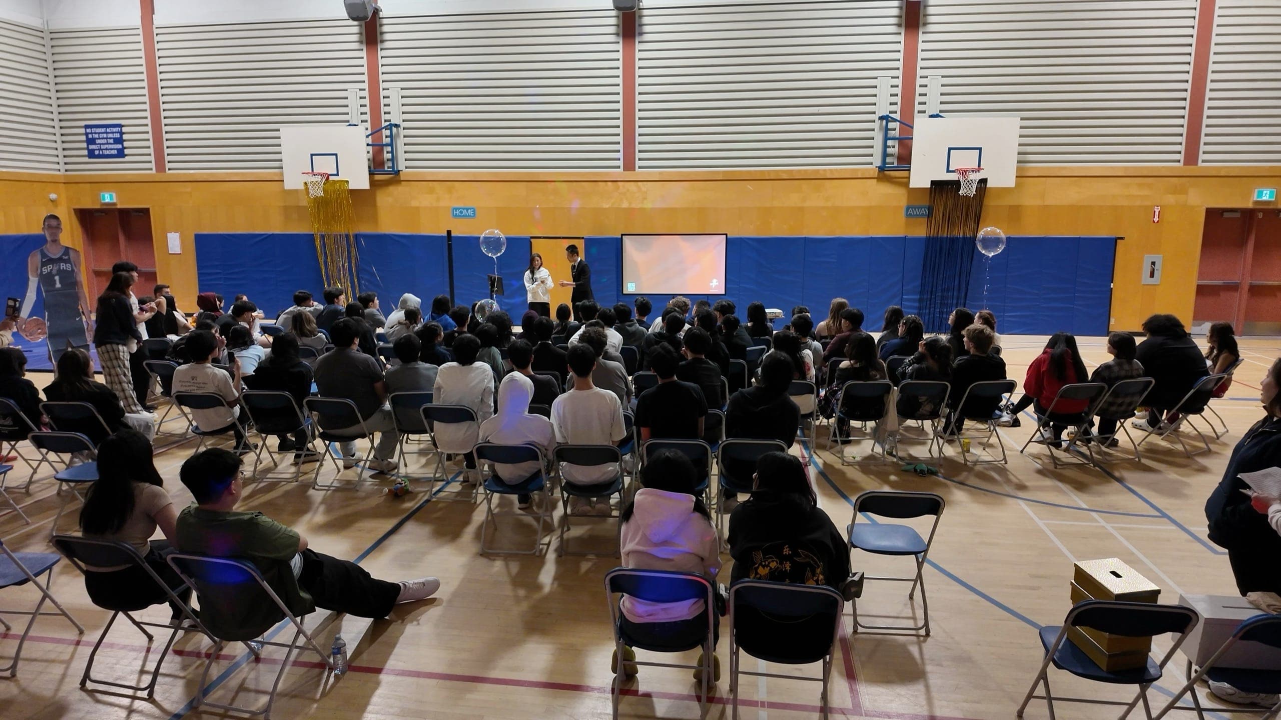 Kel performing on stage for a full gymnasium of grads at a Burnett Secondary dry grad event