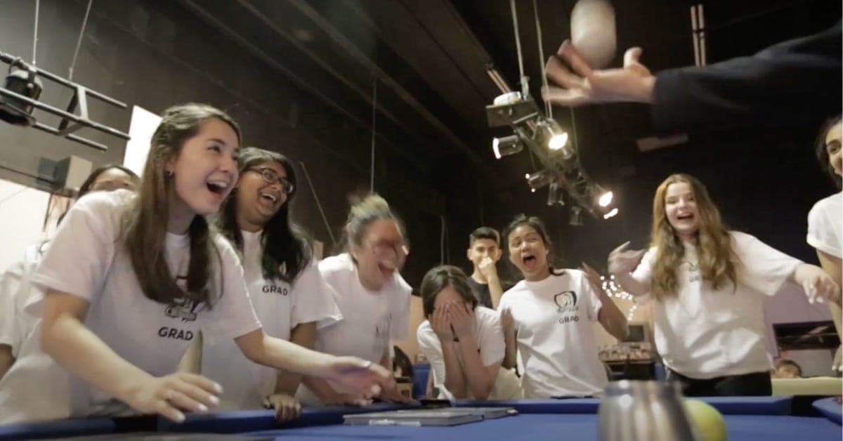 A row of students in grad shirts reacting with open-mouthed shock during a school stage show