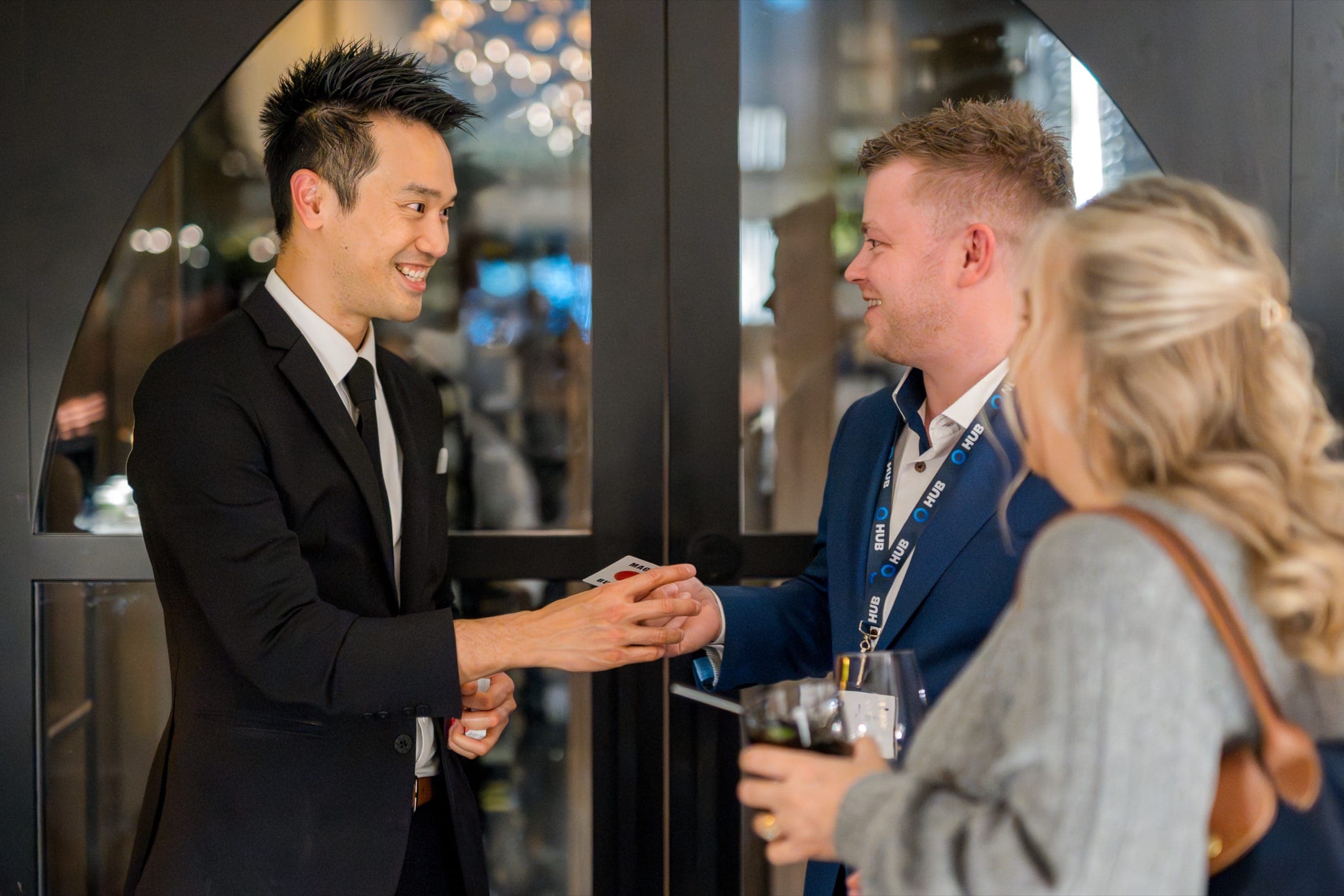 Kel handing a card to a guest in a tailored suit during a reception at a Vancouver insurance brokerage event