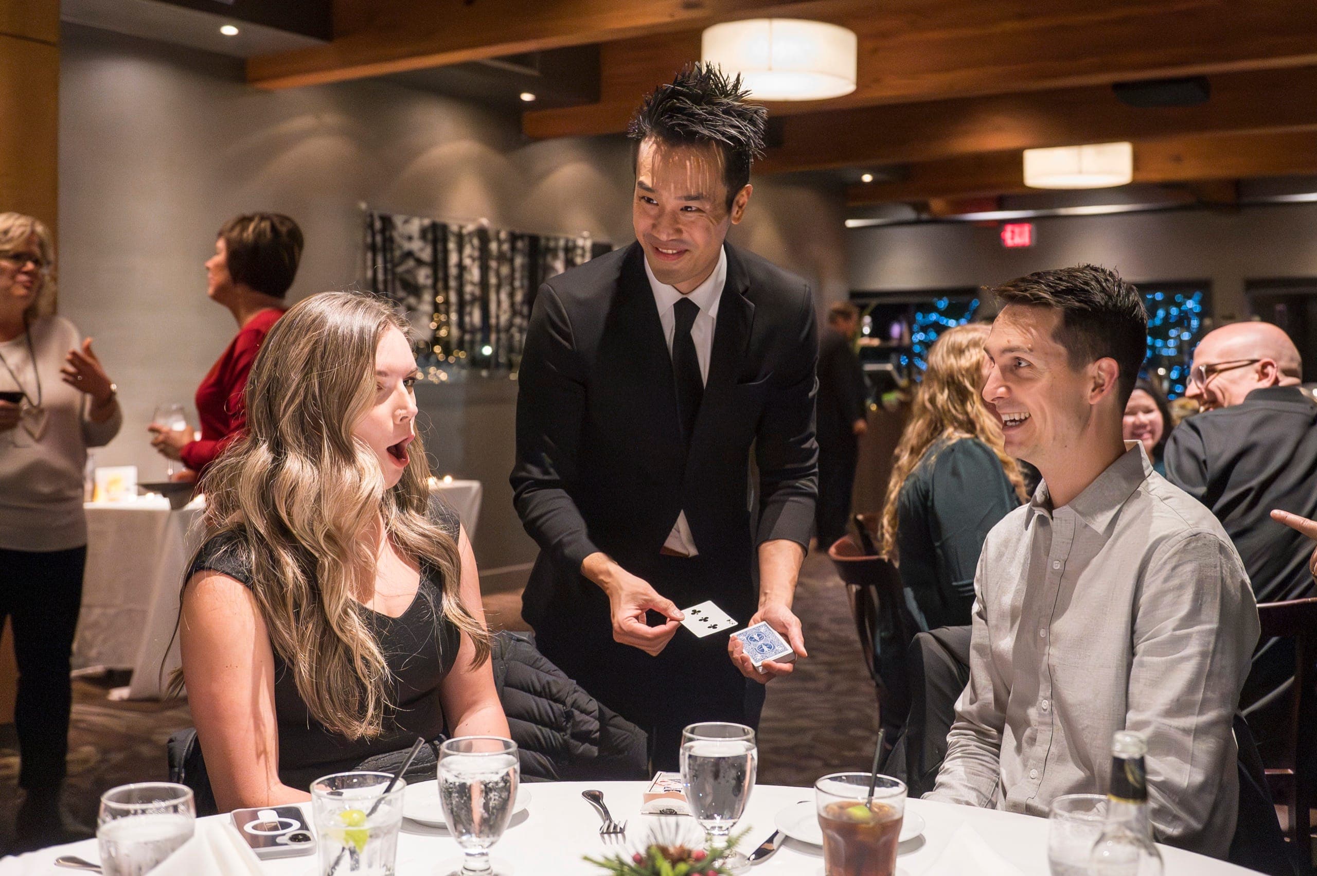 A seated guest gasping with her mouth open as Kel reveals two cards at a Vancouver client reception