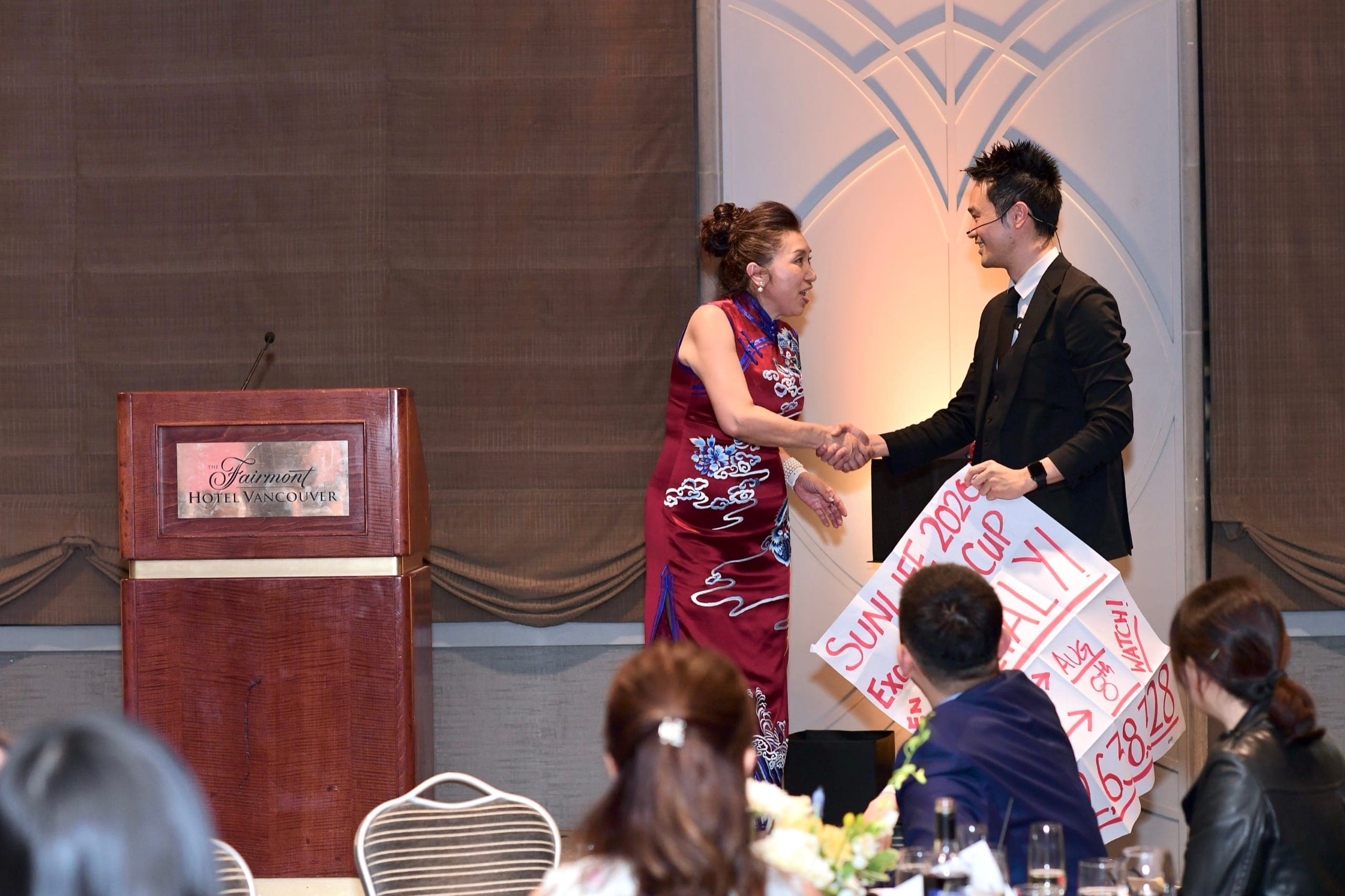 Kel shaking hands with the host on stage at the Fairmont Hotel Vancouver during a gala