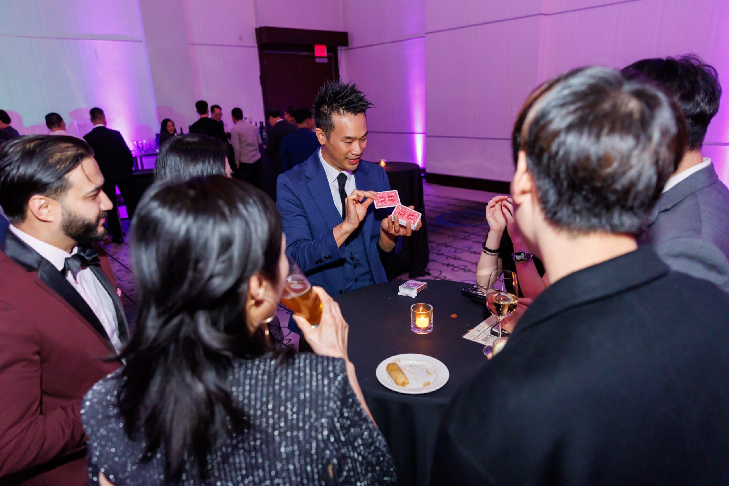 Kel showing cards to black-tie guests around a candlelit ballroom table at a Vancouver gala