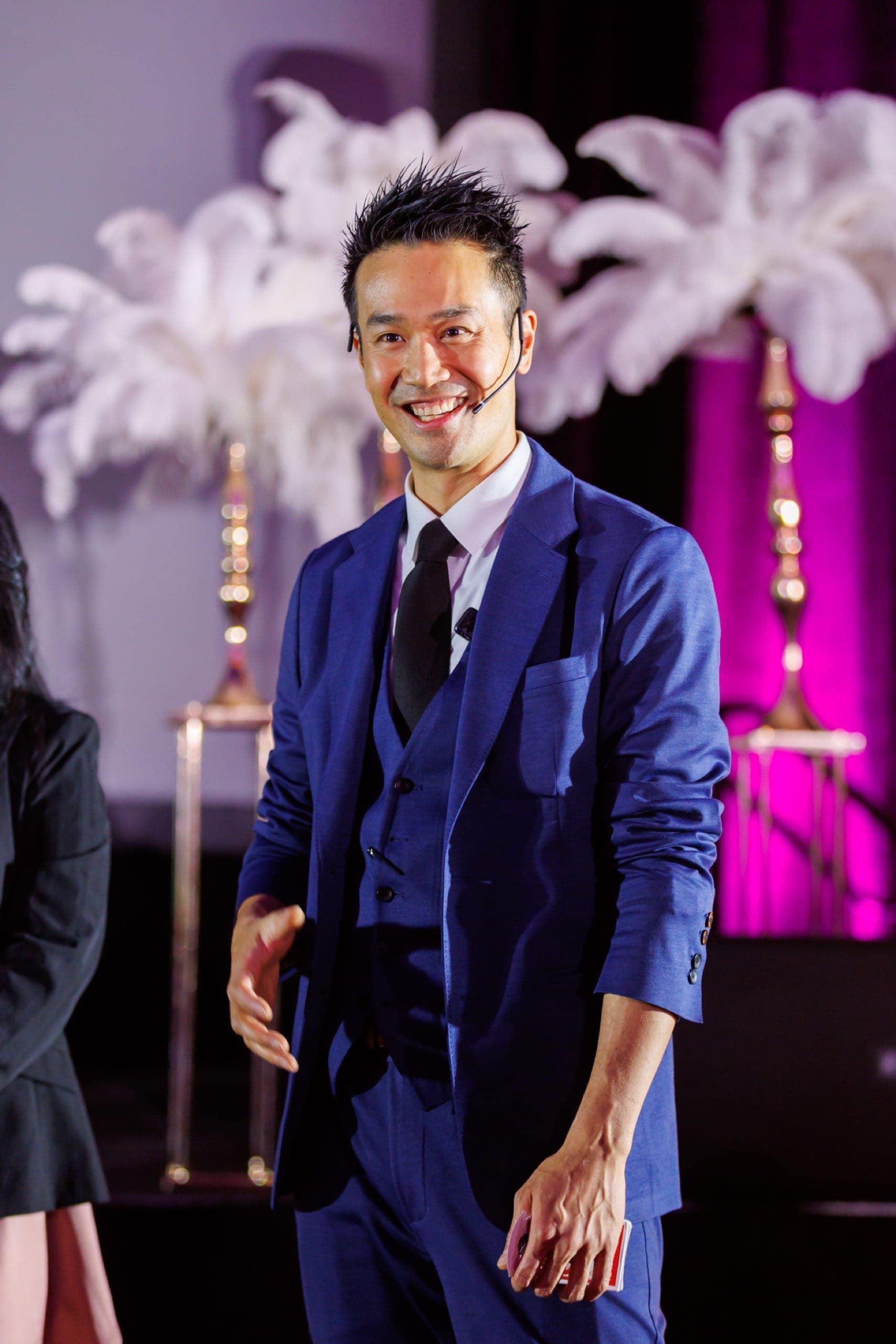 Kel walking forward into the room with a headset microphone while hosting a Vancouver gala