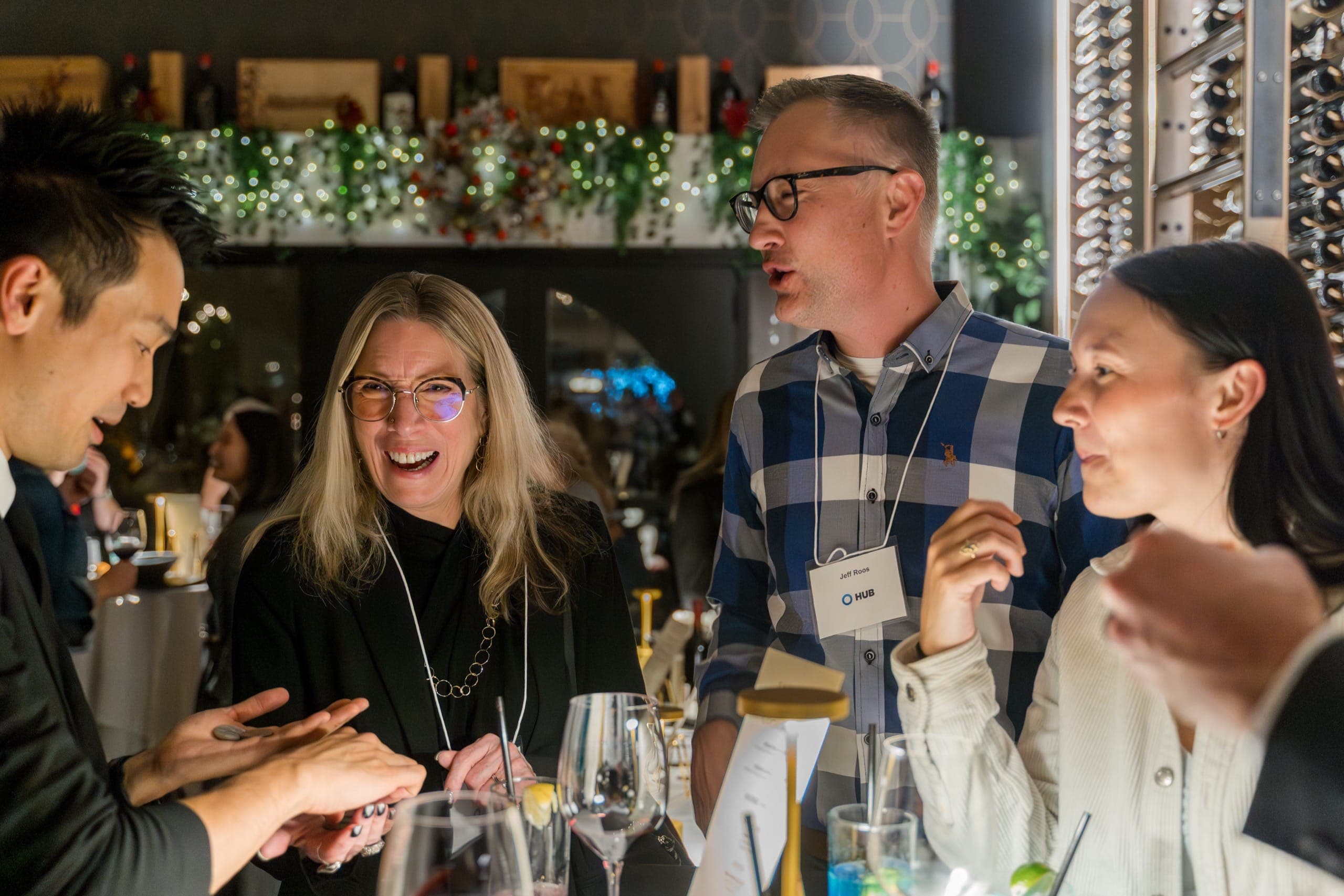 Guests laughing during close-up magic under Christmas garland at a corporate holiday party