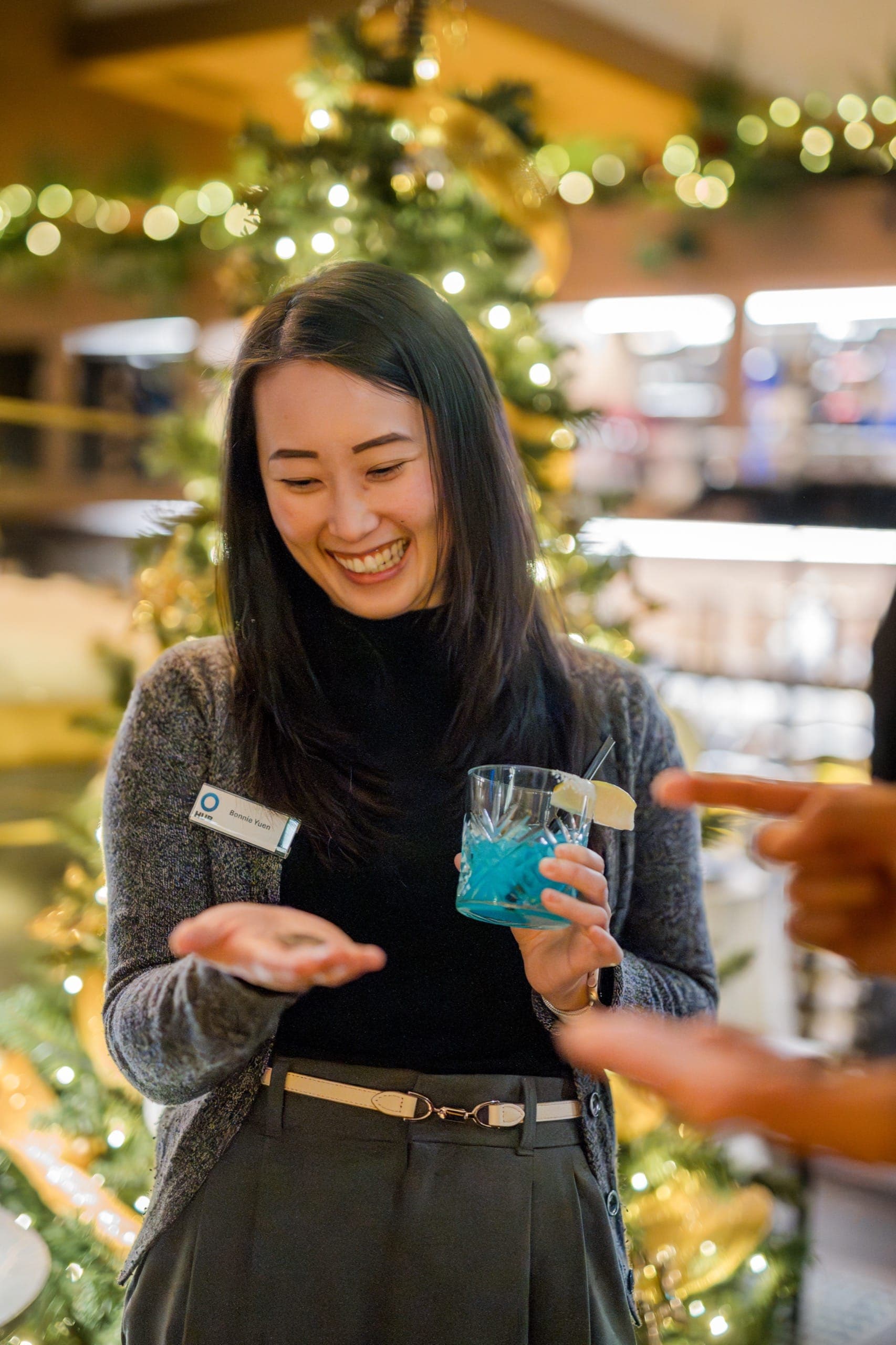 A guest smiling down at a coin resting on her own palm in front of a lit Christmas tree at a Vancouver holiday party
