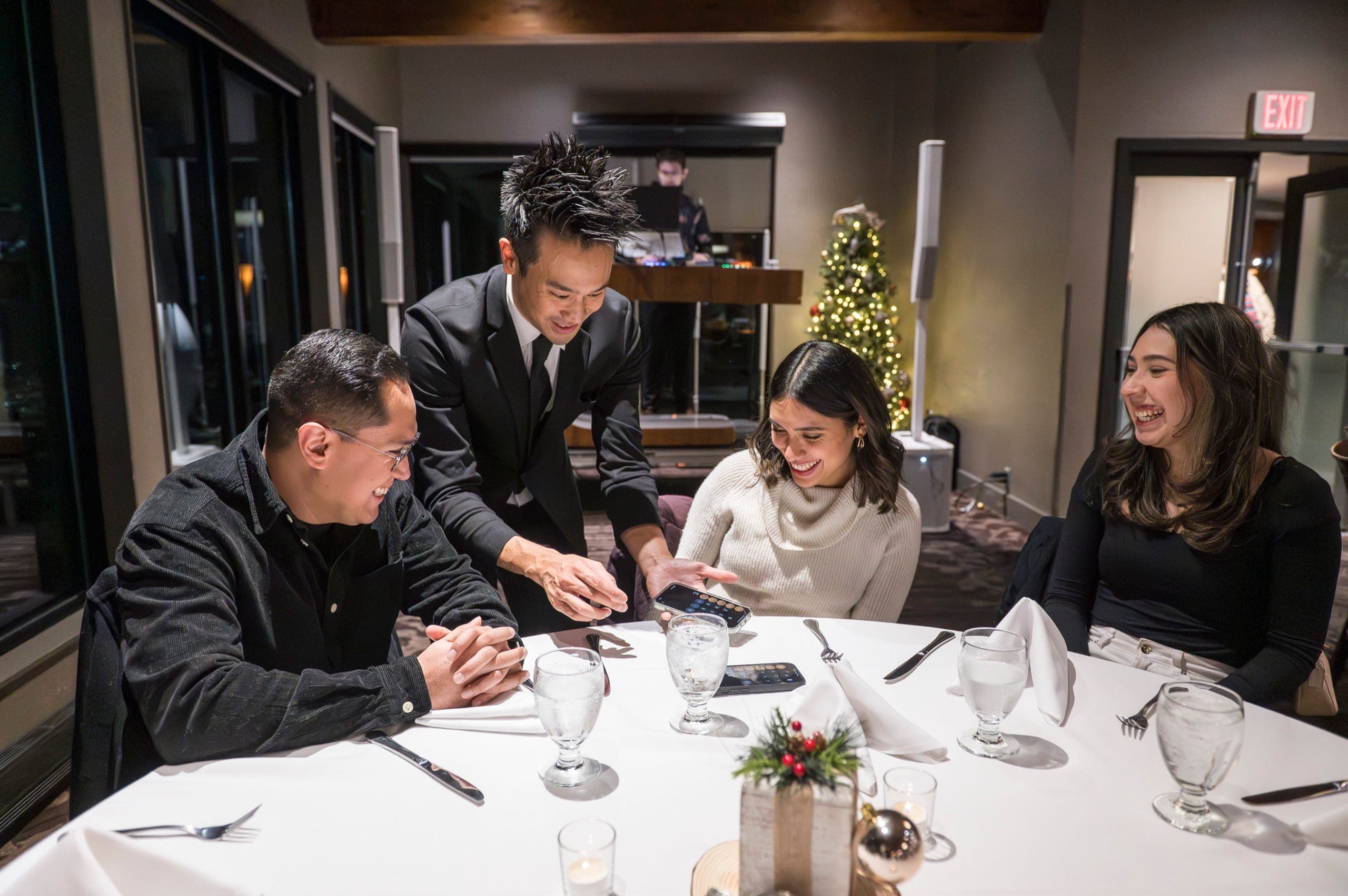 A table of four laughing together during close-up card magic at a Vancouver holiday party