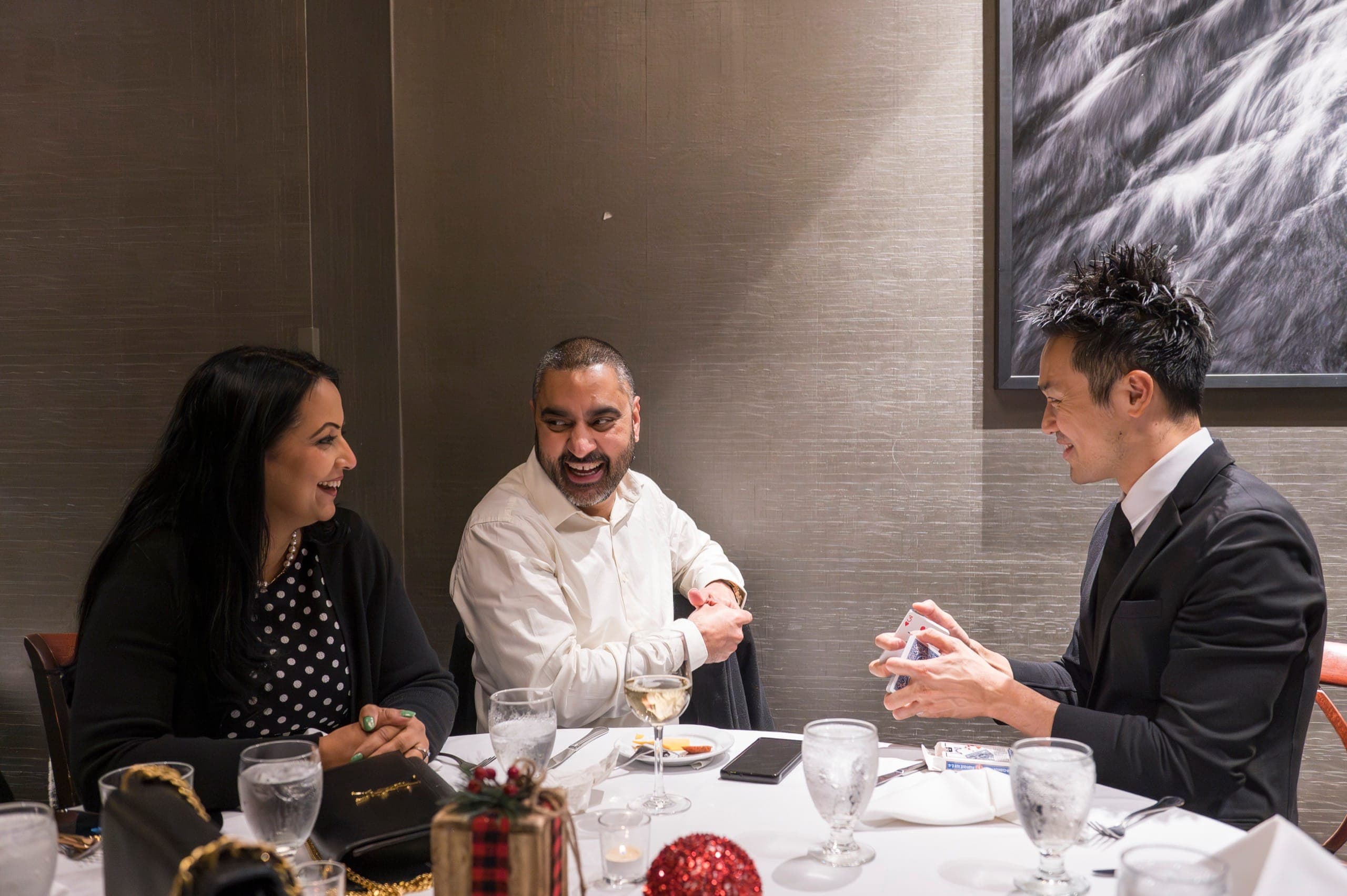A table of guests laughing hard during close-up card magic at a Vancouver firm dinner