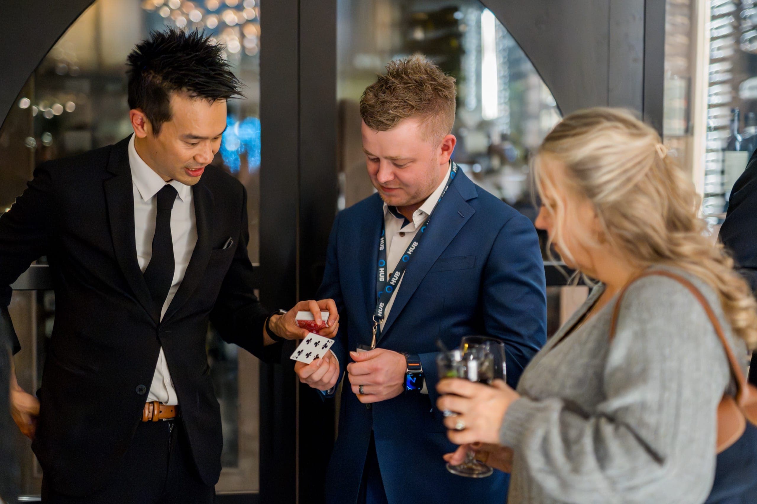 Kel showing a card to two guests during a corporate reception, drinks in hand