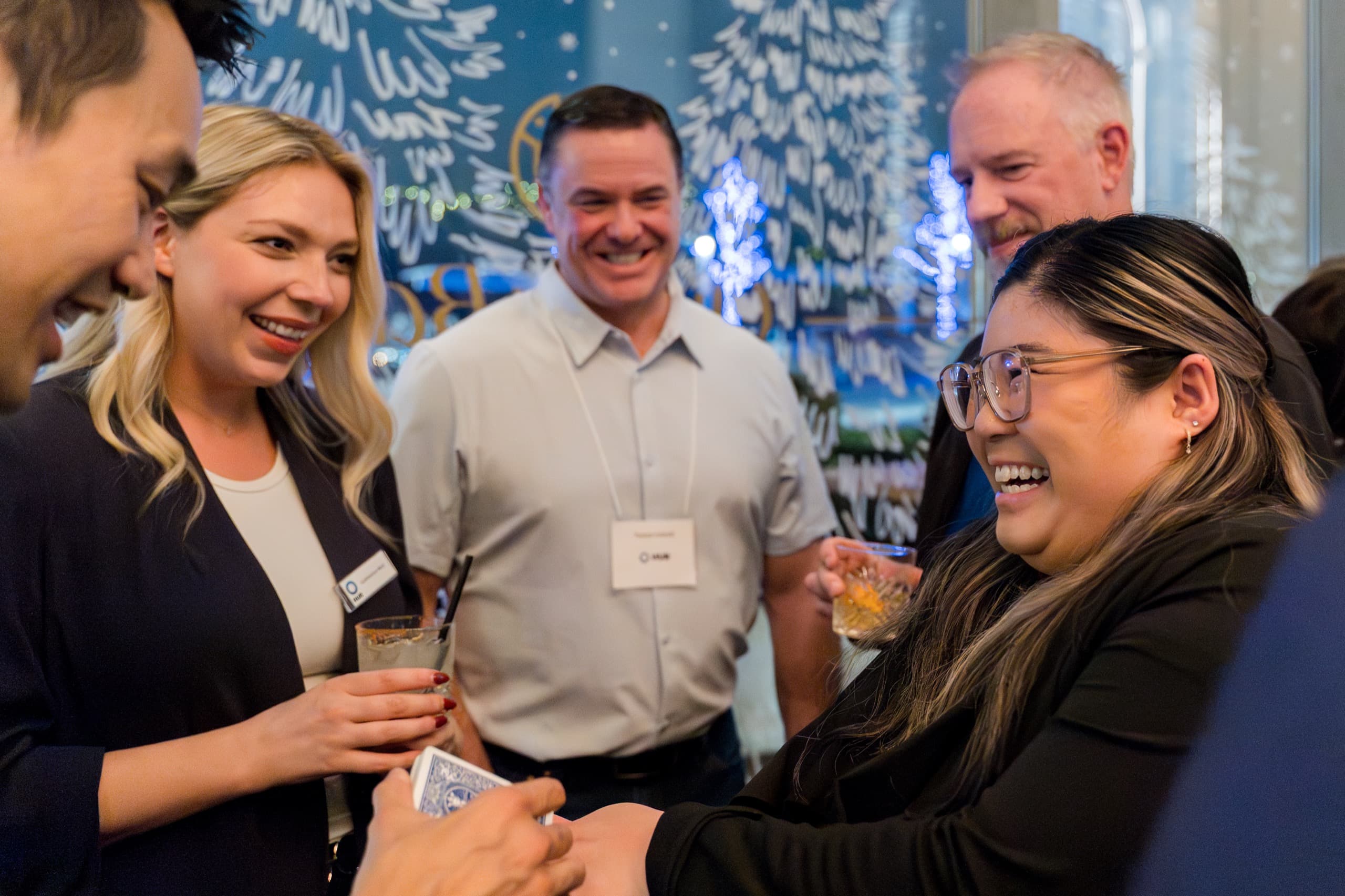 Guests wearing conference name badges laughing together during close-up card magic at a corporate reception