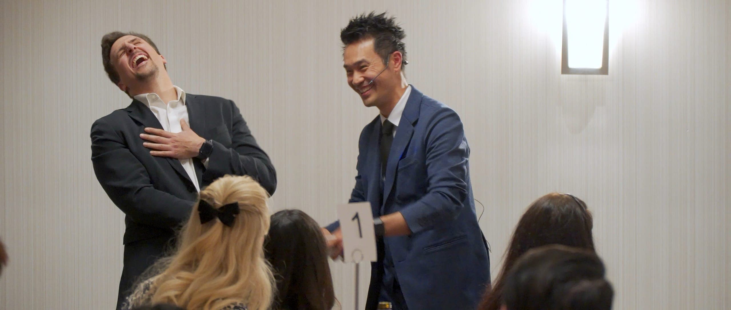 A guest laughing hard on stage beside Kel during an MC segment at a Vancouver corporate event