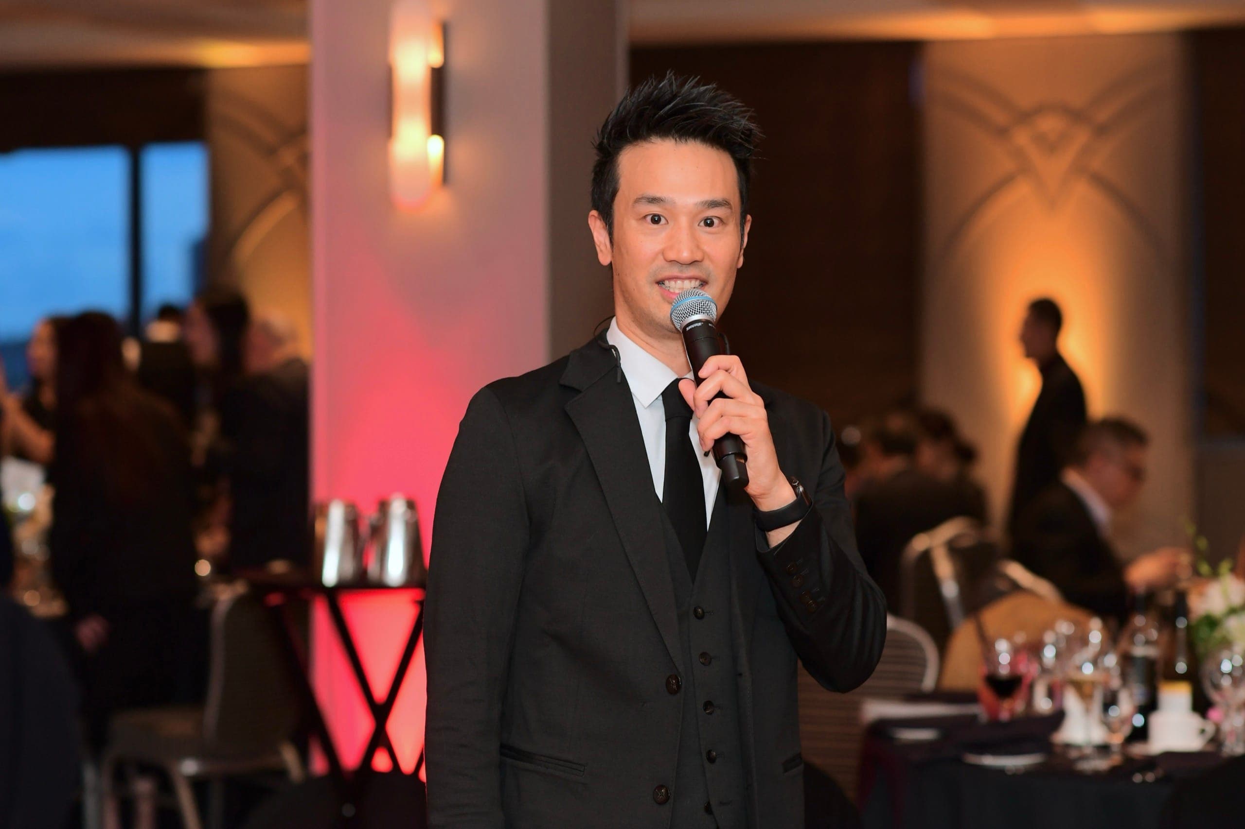 Kel hosting with a handheld microphone in front of a full ballroom at a Vancouver corporate awards night