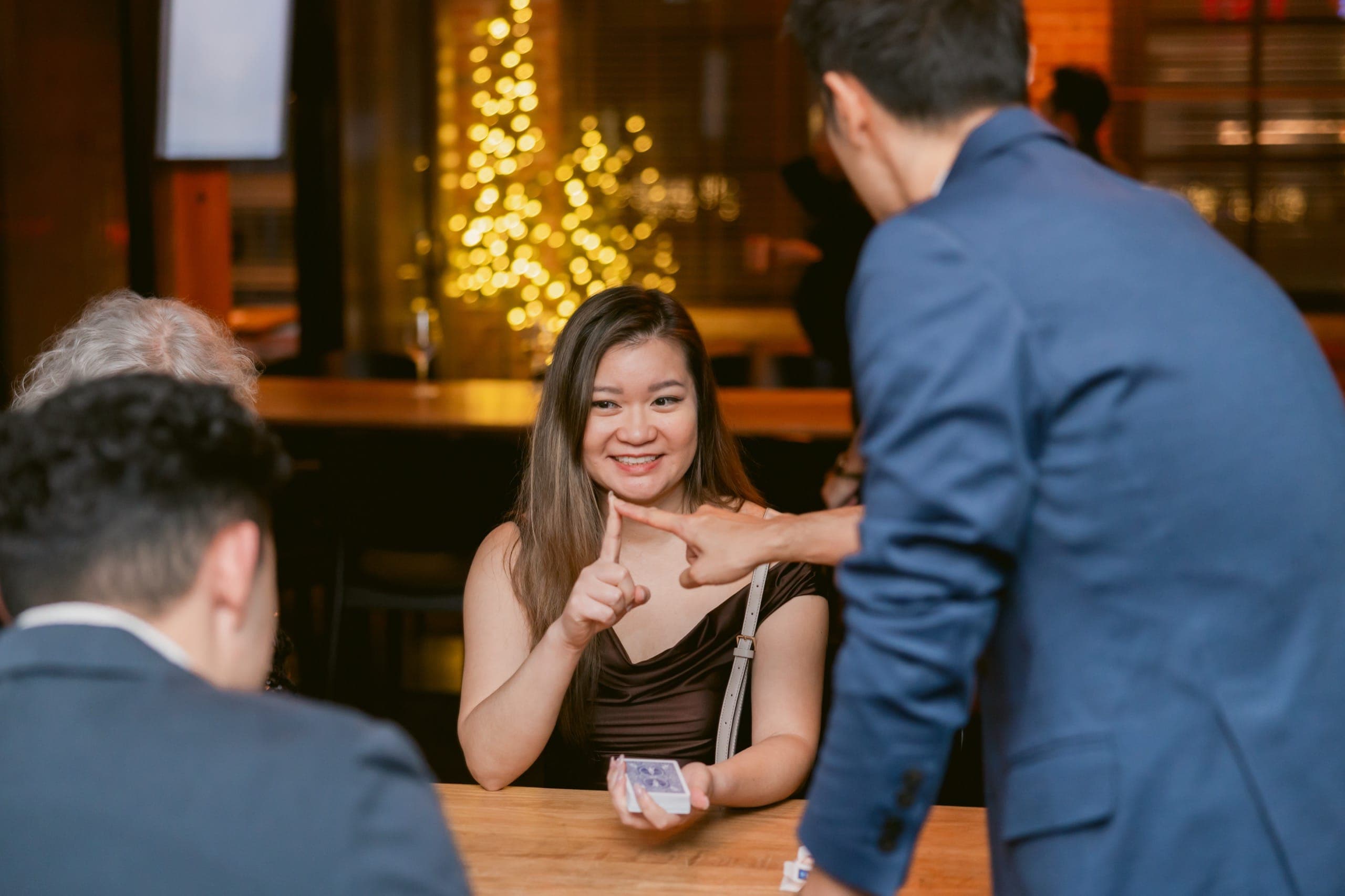 A guest beaming at Kel across the bar with a lit Christmas tree behind her at a Vancouver holiday party