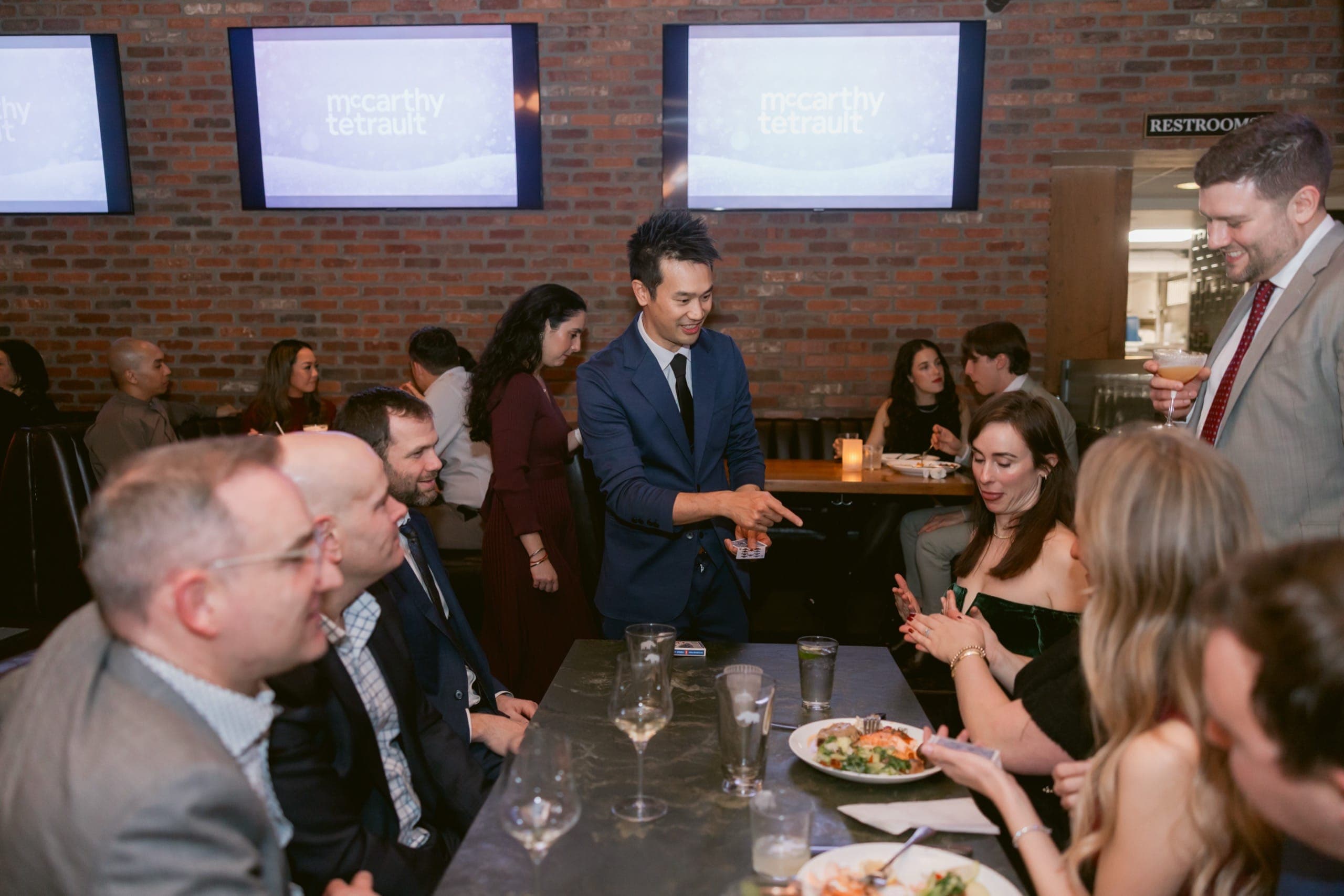 A packed room of guests down a long table watching close-up magic at a Vancouver law firm holiday party