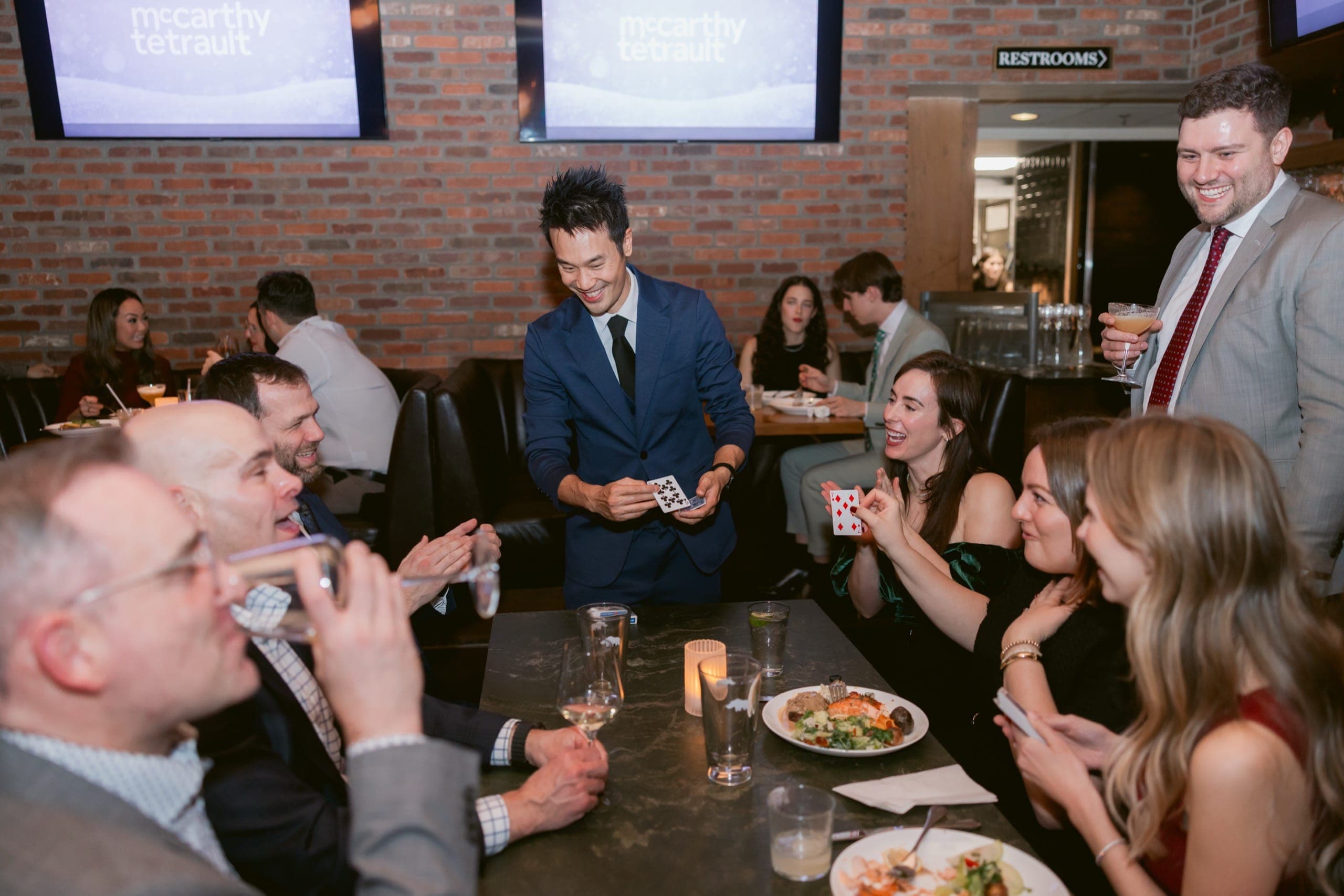 A full table erupting in laughter during close-up card magic at the McCarthy Tetrault holiday party in Vancouver