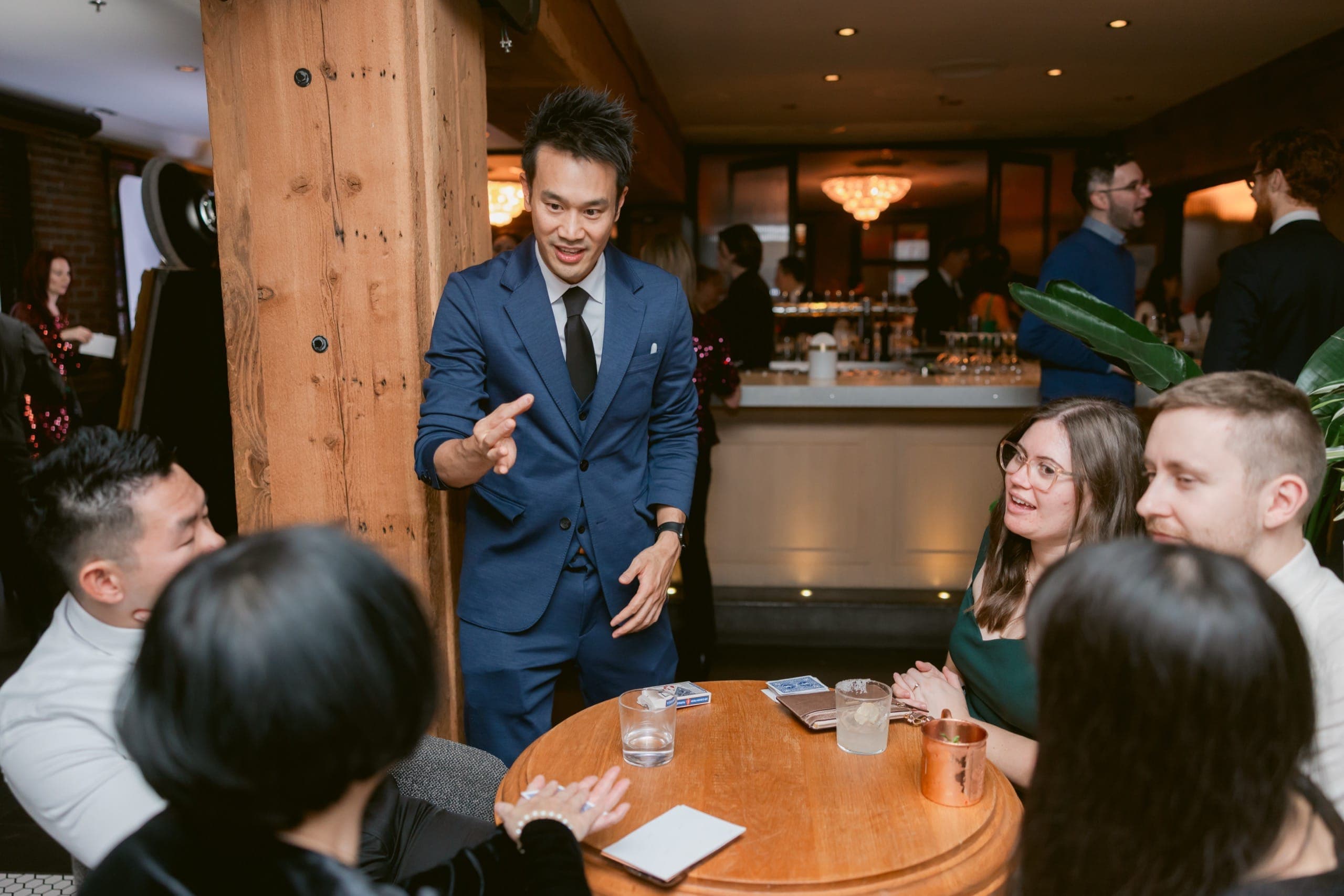 Kel standing mid-room working a table of guests during a corporate reception