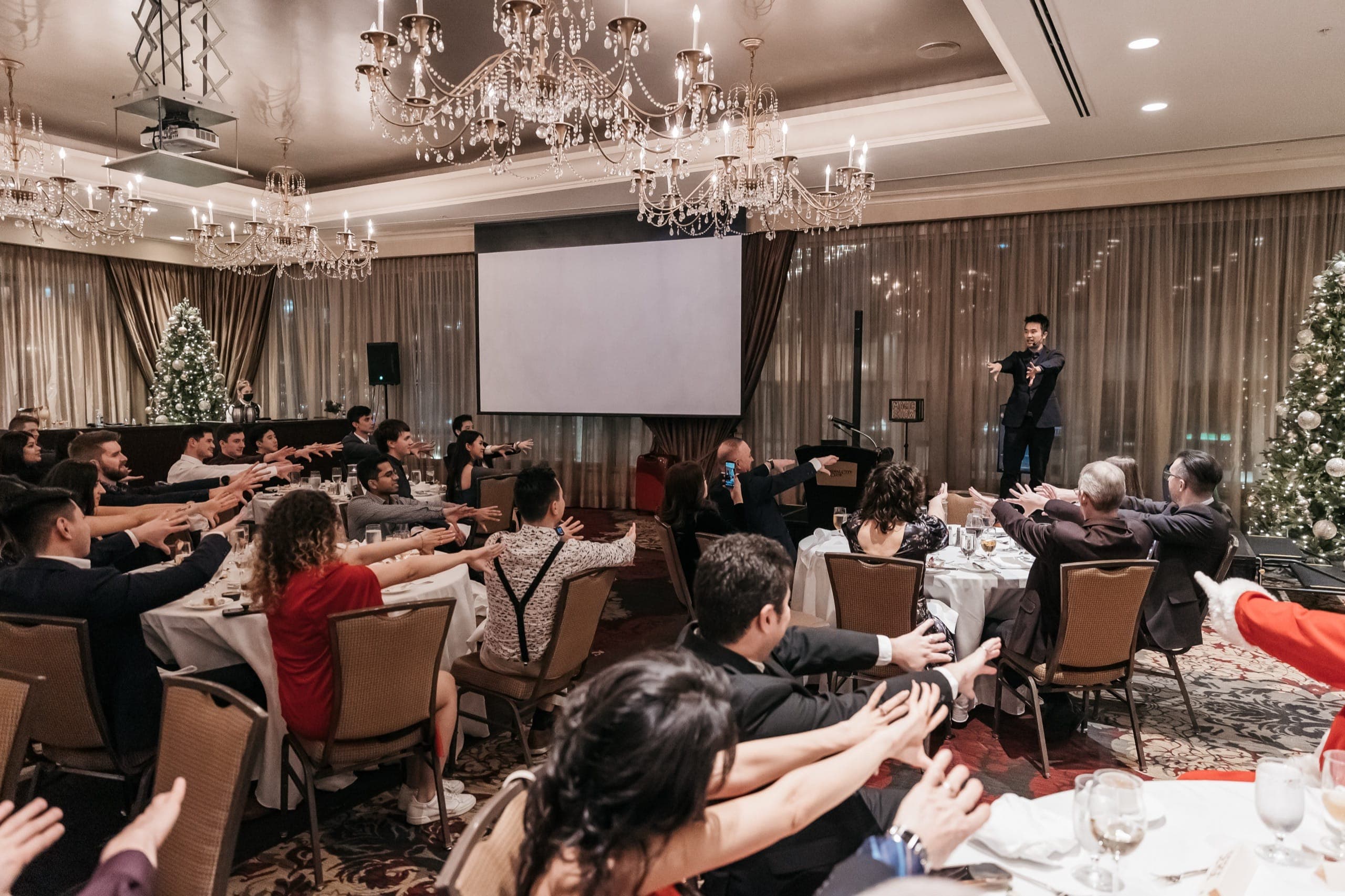 A chandelier ballroom of guests holding their arms out in unison during a mentalism routine in Vancouver