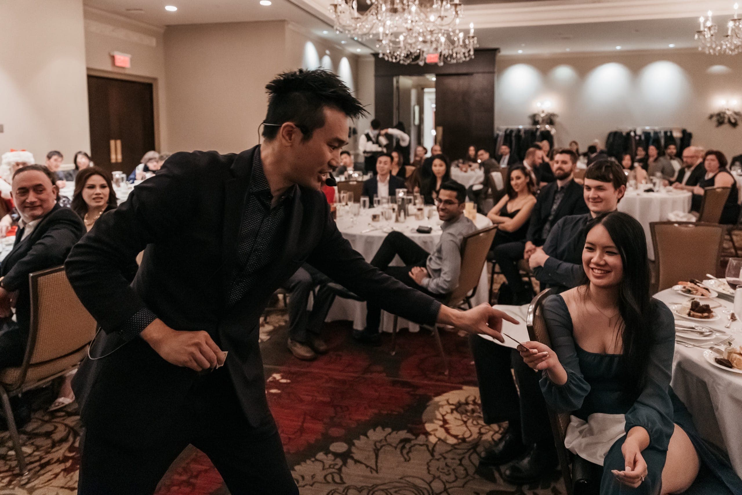 Kel leaning off the stage to hand a card to a grinning guest during a Vancouver corporate show