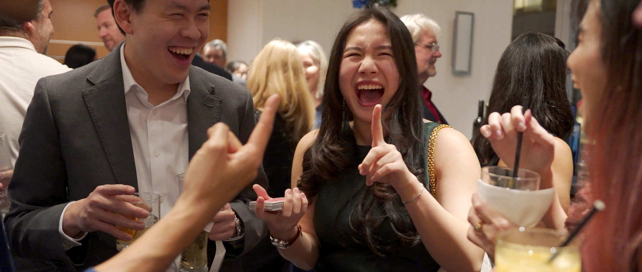 Two guests laughing and pointing in disbelief during close-up magic at a Vancouver mining company reception