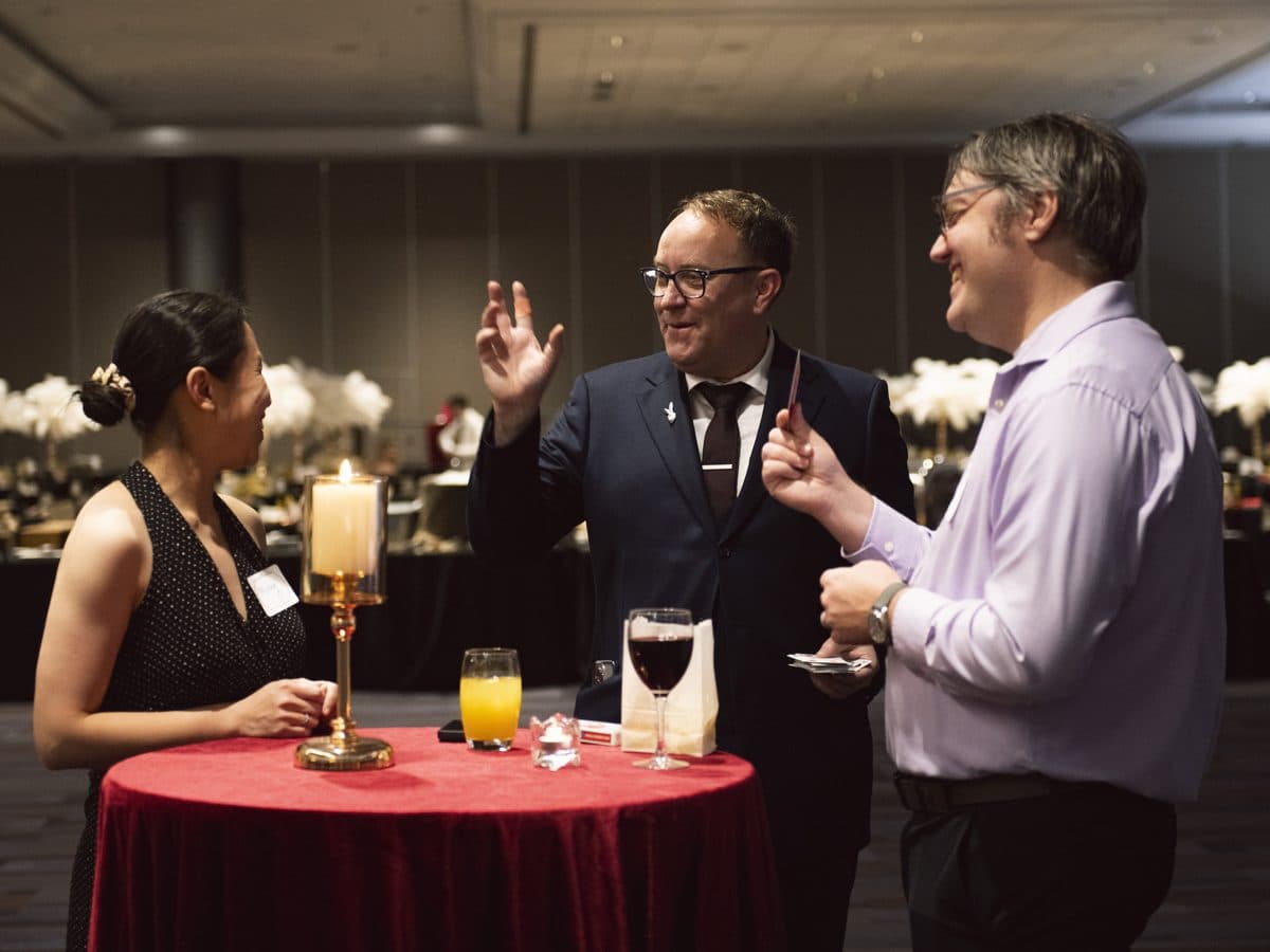 Bro Gilbert performing close-up magic for two guests at a cocktail table during a ballroom event