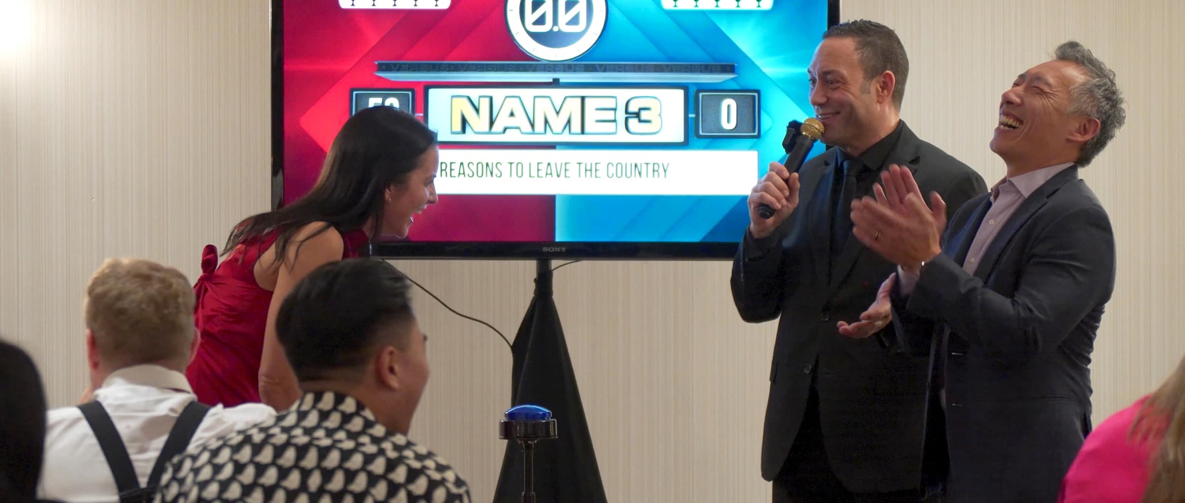 Mike Oulton hosting a buzzer game at Endeavour Silver, the Name 3 scoreboard on screen and two contestants laughing at the buzzer