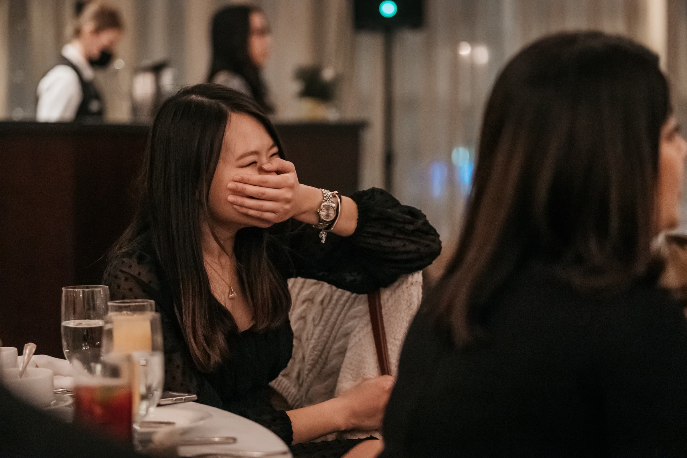A guest at a banquet table with her hand over her mouth, laughing during dinner at a Vancouver corporate event