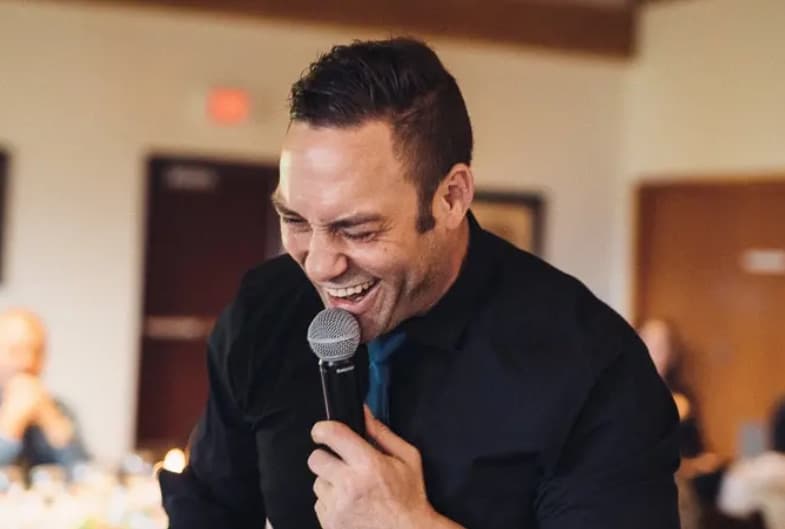 Mike Oulton laughing with his head back into a handheld microphone while hosting a Vancouver event