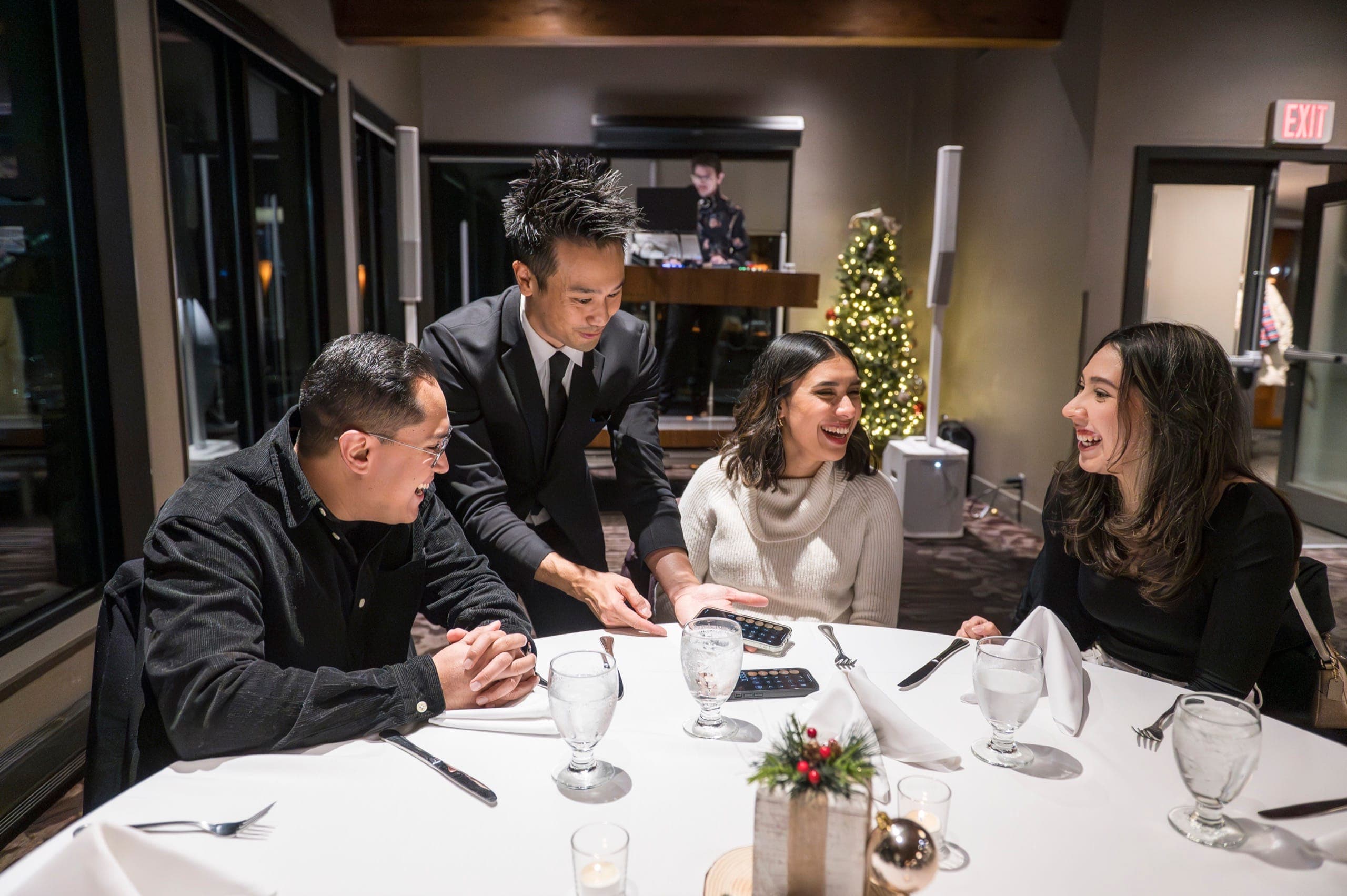 Kel performing a routine on a guest's palm while the table laughs at a Vancouver industry event