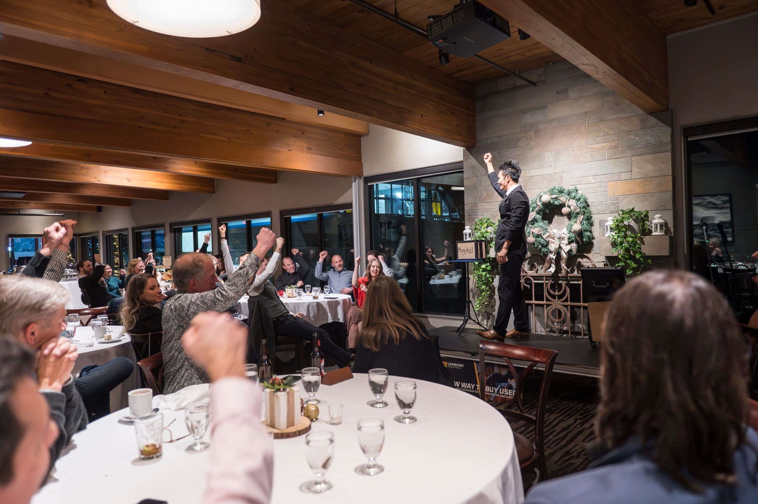 A full room with fists punched in the air cheering back at Kel on stage at a Vancouver corporate event