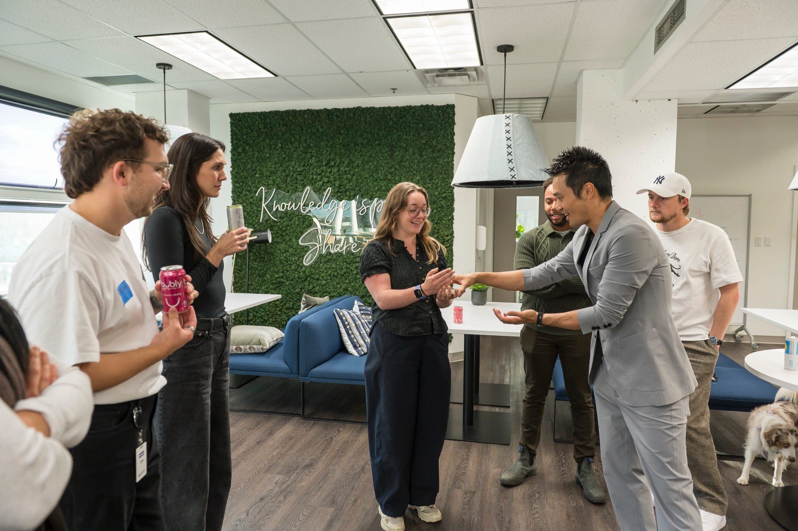 Colleagues standing with drinks and name badges watching close-up magic at a Vancouver tech company social