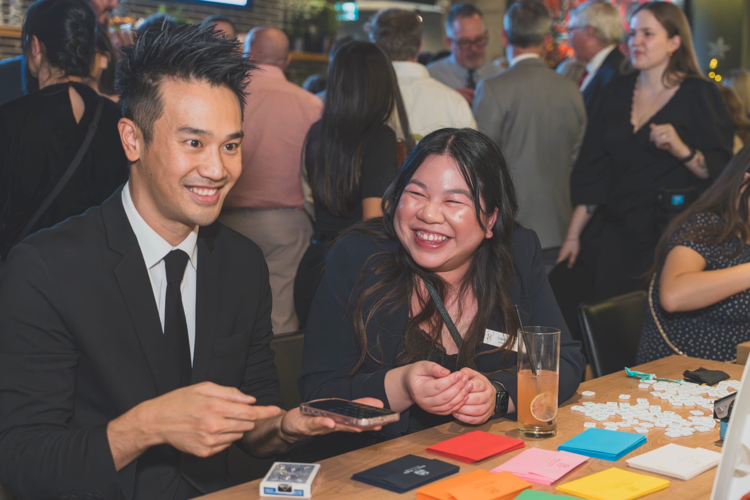 Coworkers laughing during a table-side card effect at a Vancouver tech company holiday party