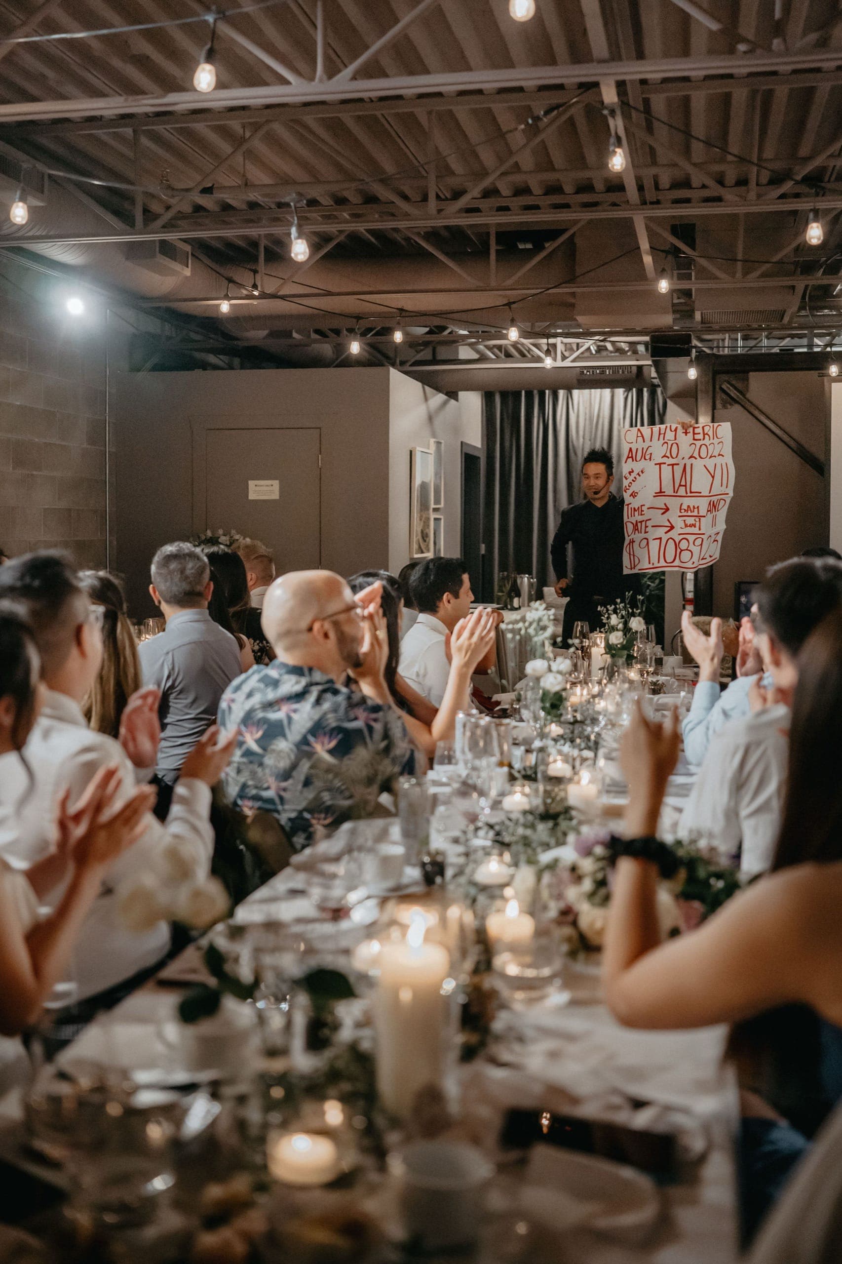 Kel revealing a written prediction to a cheering wedding reception at Cathy and Eric's Vancouver wedding