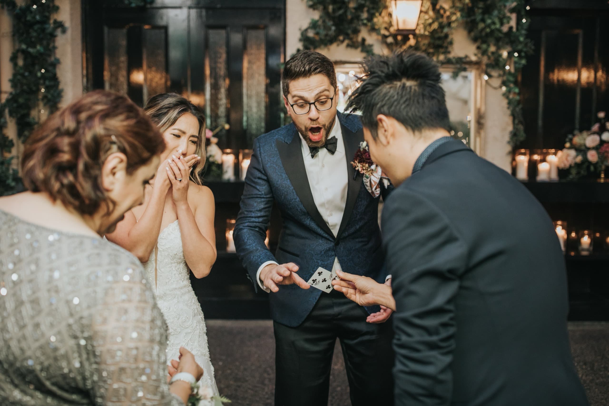 A groom with his jaw dropped and the bride's hands over her mouth during close-up card magic at their Vancouver wedding