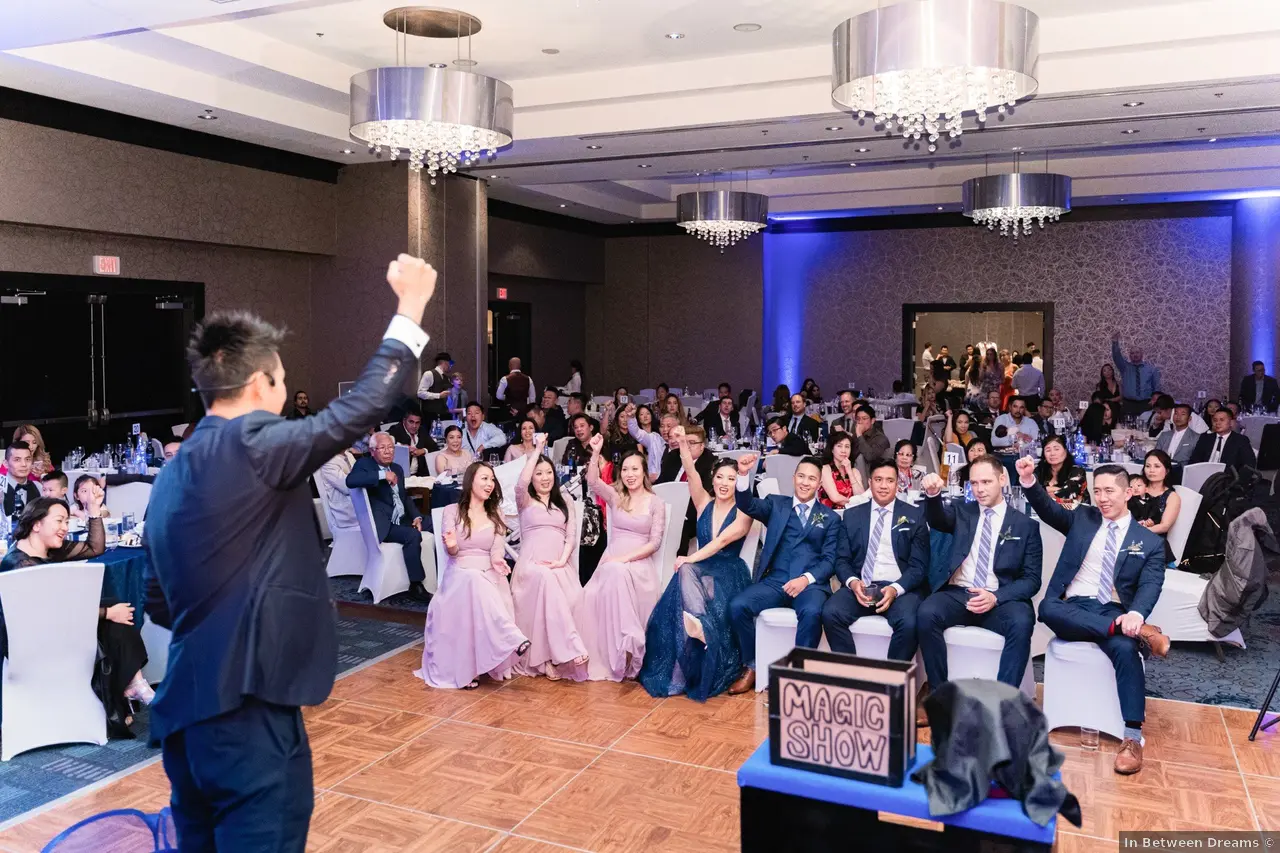 Jason and Tam's entire bridal party cheering with fists raised during Kel's magic show at their Vancouver wedding