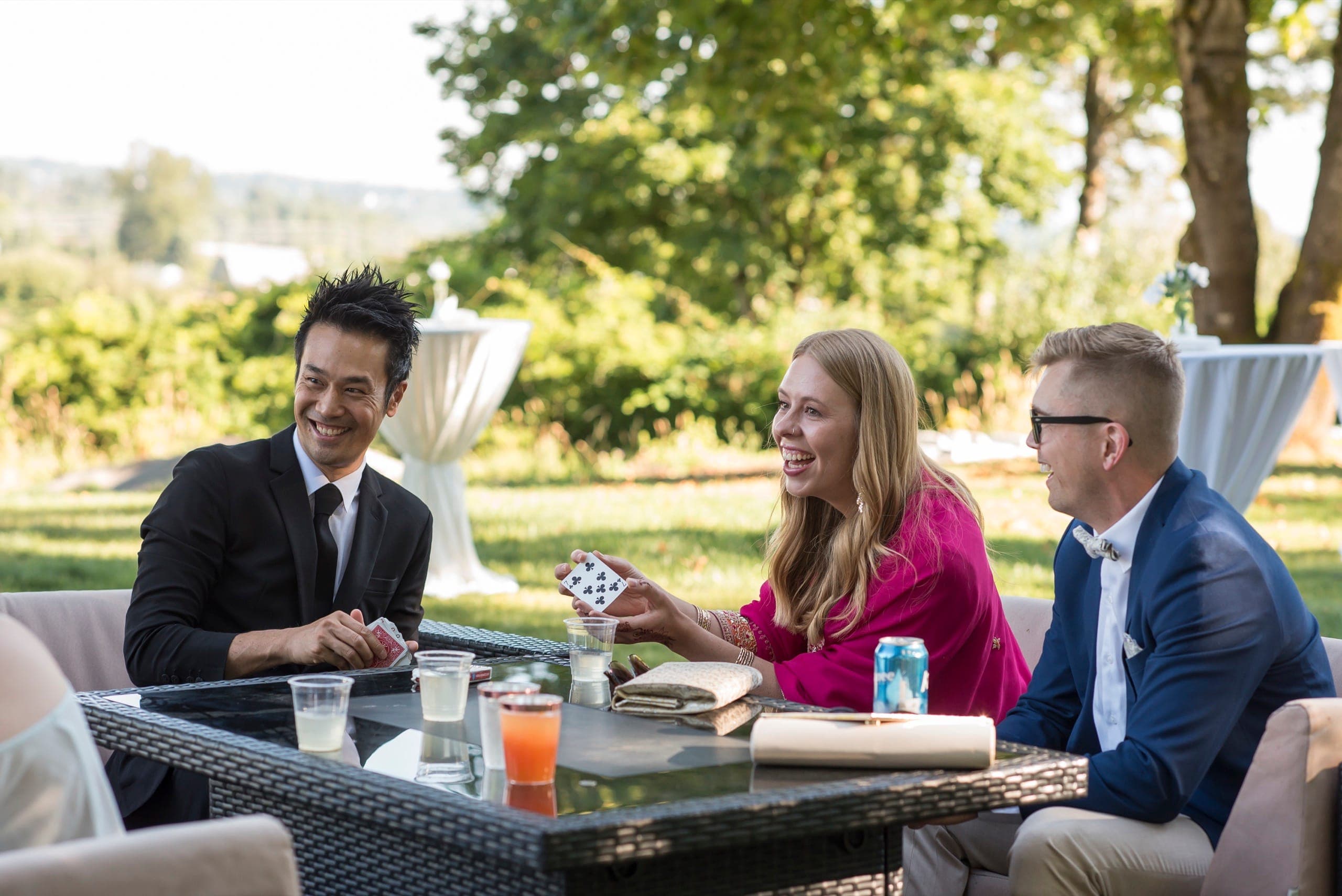Wedding guests laughing during close-up card magic at an outdoor Vancouver cocktail hour