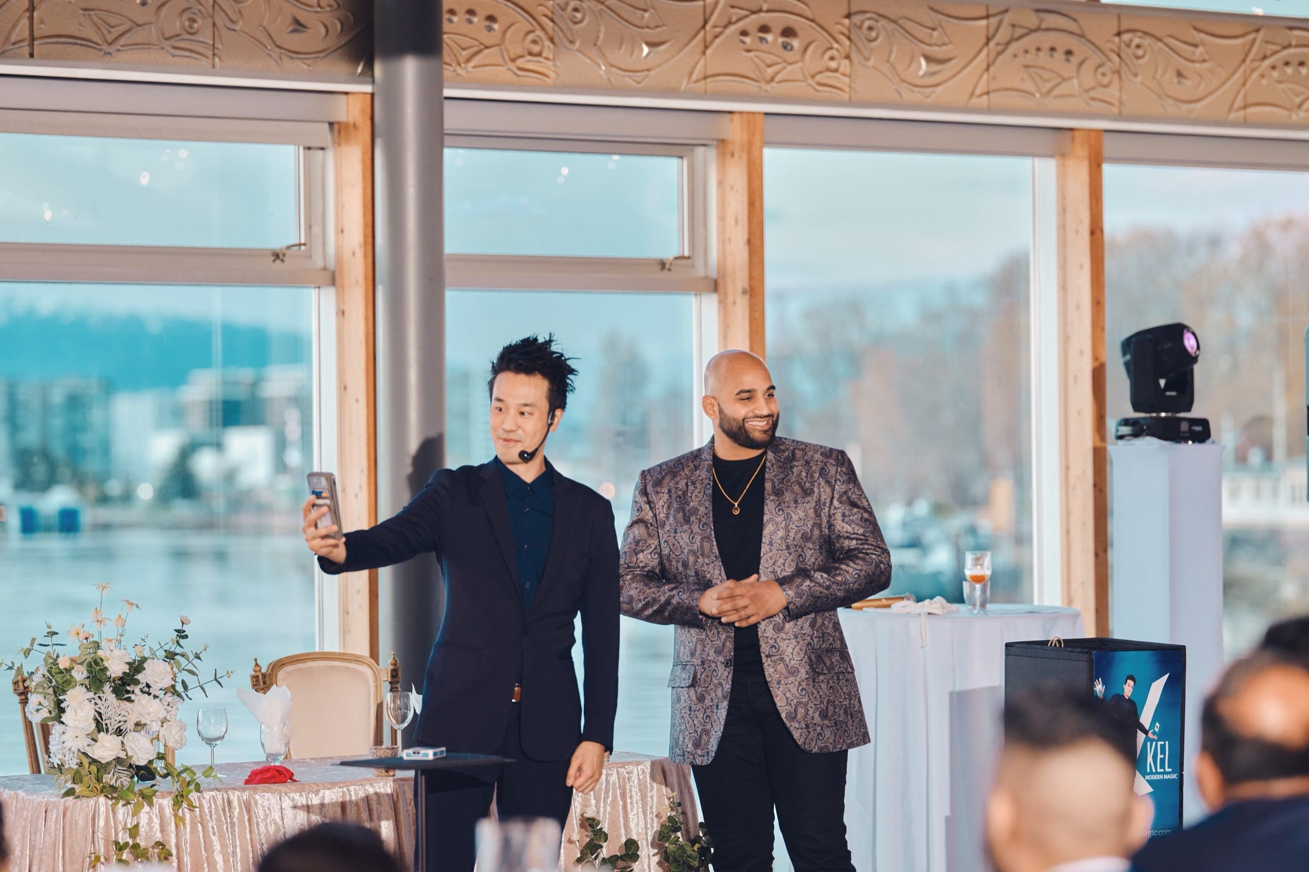 Kel laughing while filming a wedding guest's reaction on his phone during a close-up magic routine