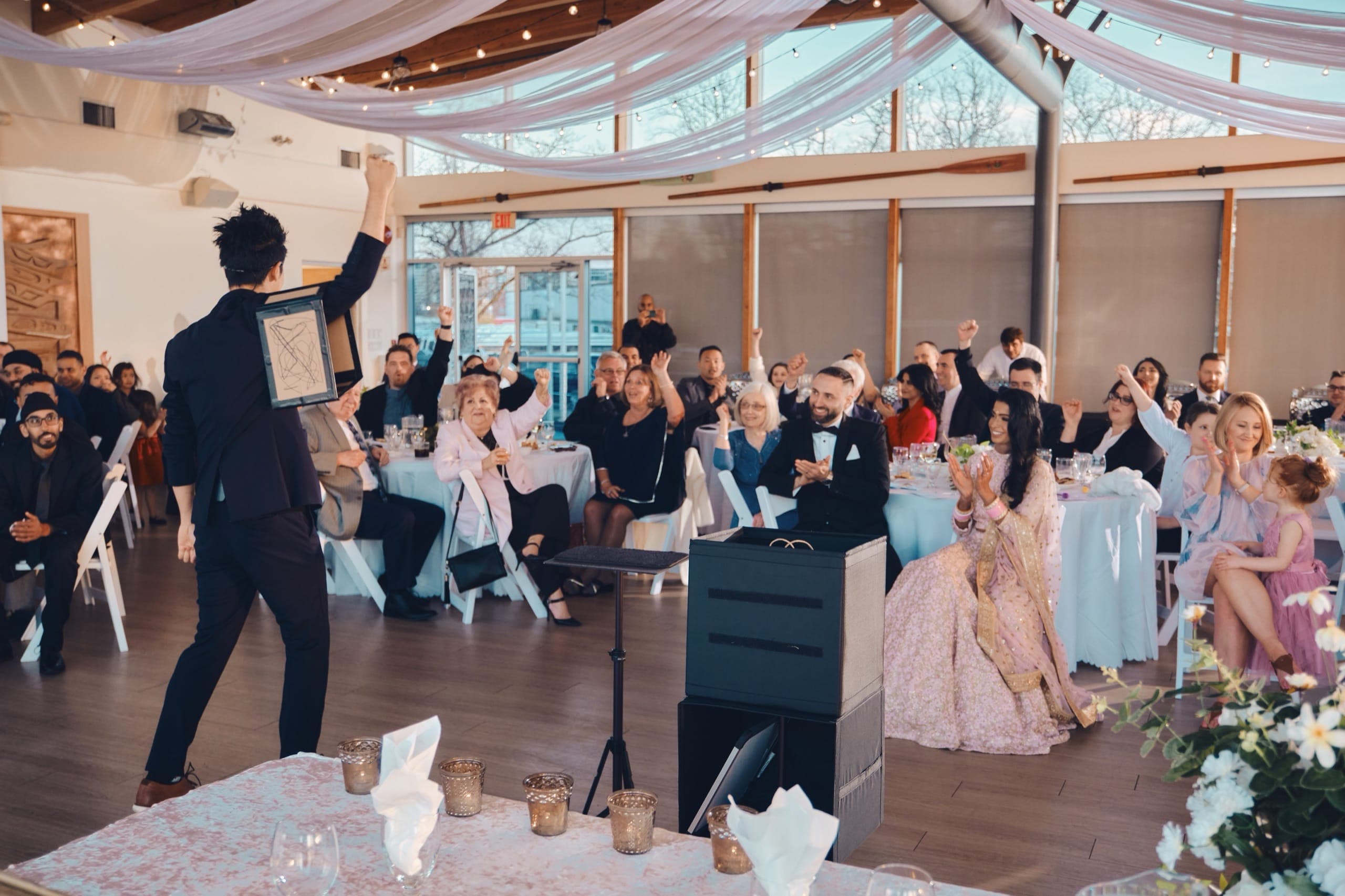 Kel revealing a prediction to a cheering wedding reception, bride and groom applauding
