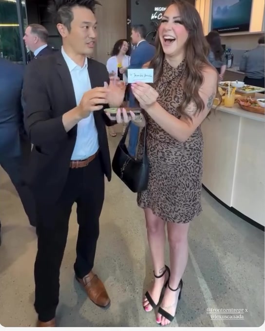 A guest laughing as she holds up a card next to Kel at the Studio by Regency Lexus grand opening