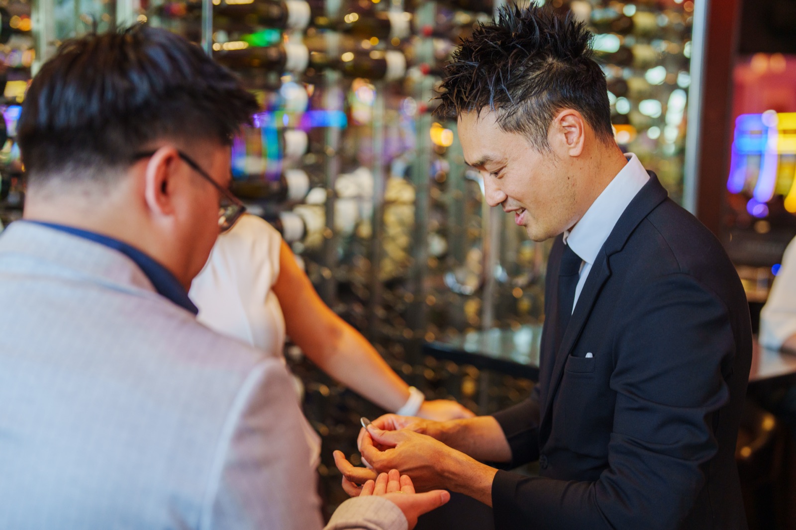 Kel performing close-up magic in a guest's hands beside the wine wall at ATLAS Steak + Fish, Grand Villa Casino