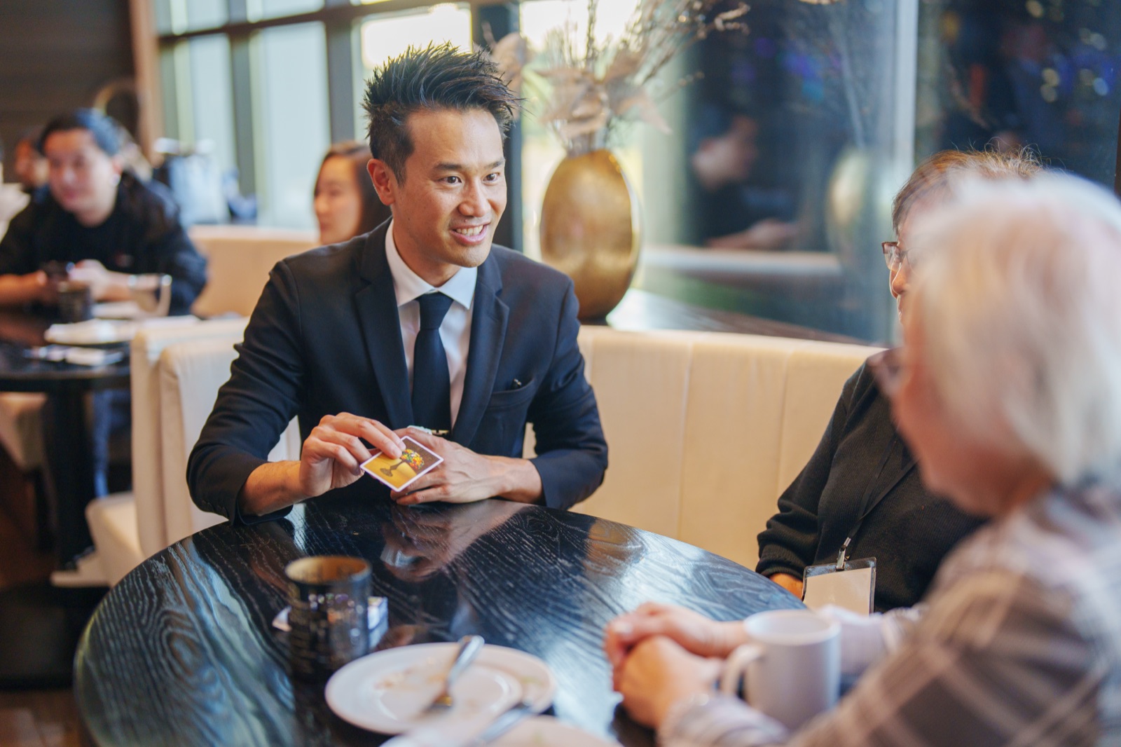 Kel performing card magic table-side for a guest at BCLC's VIP dinner at ATLAS Steak + Fish in Burnaby