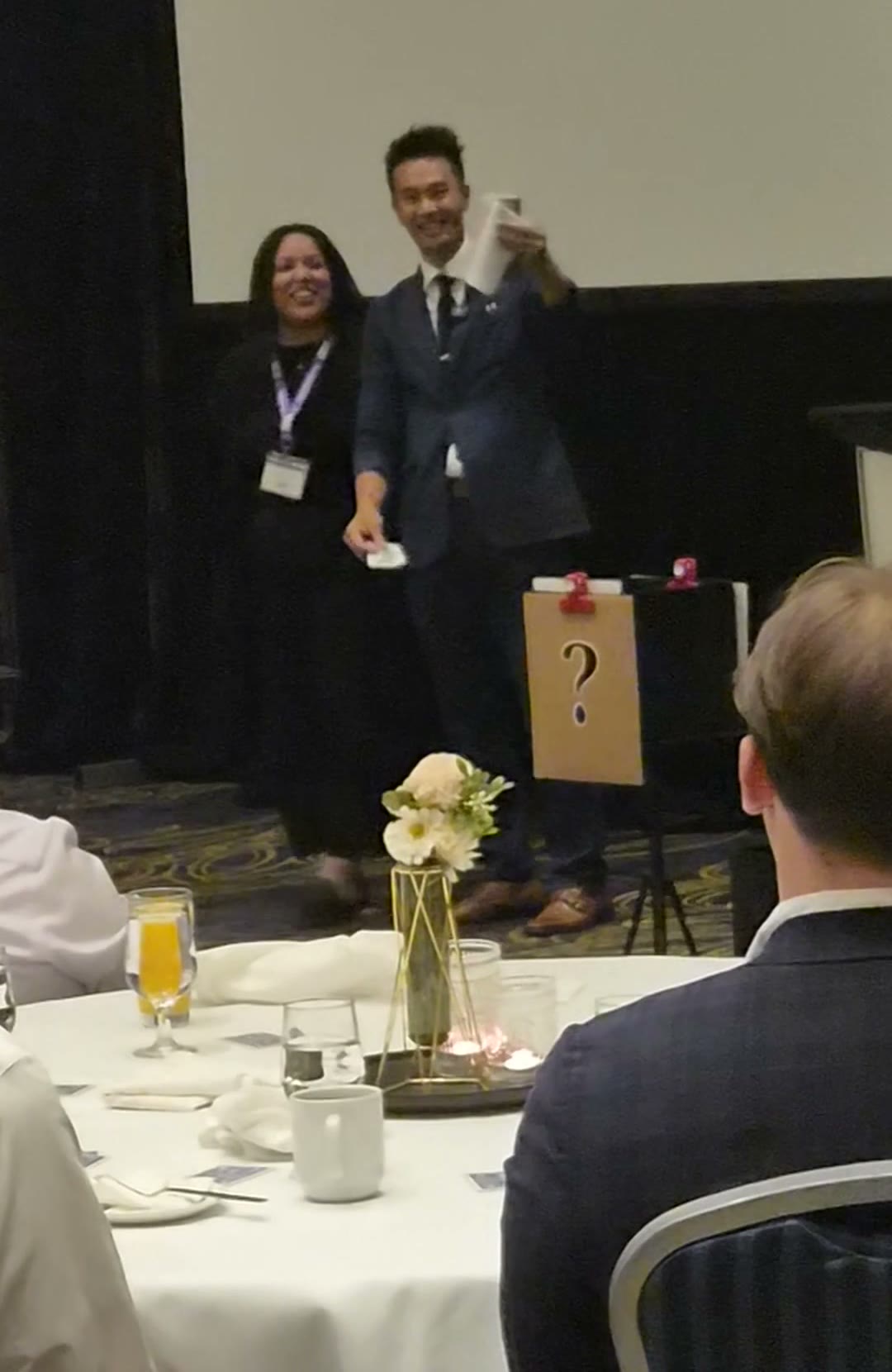 A Beem Wealth volunteer laughing on stage beside Kel during the feature show at the Delta Hotels, Grand Villa Casino